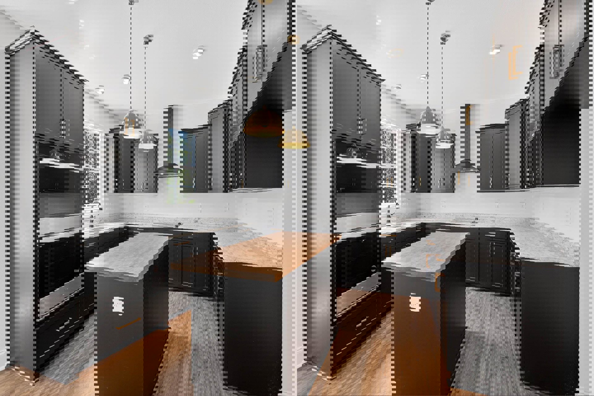 Black kitchen cabinets, wood flooring, wooden island countertop, stainless steel oven, microwave, white electrical outlet on black backsplash