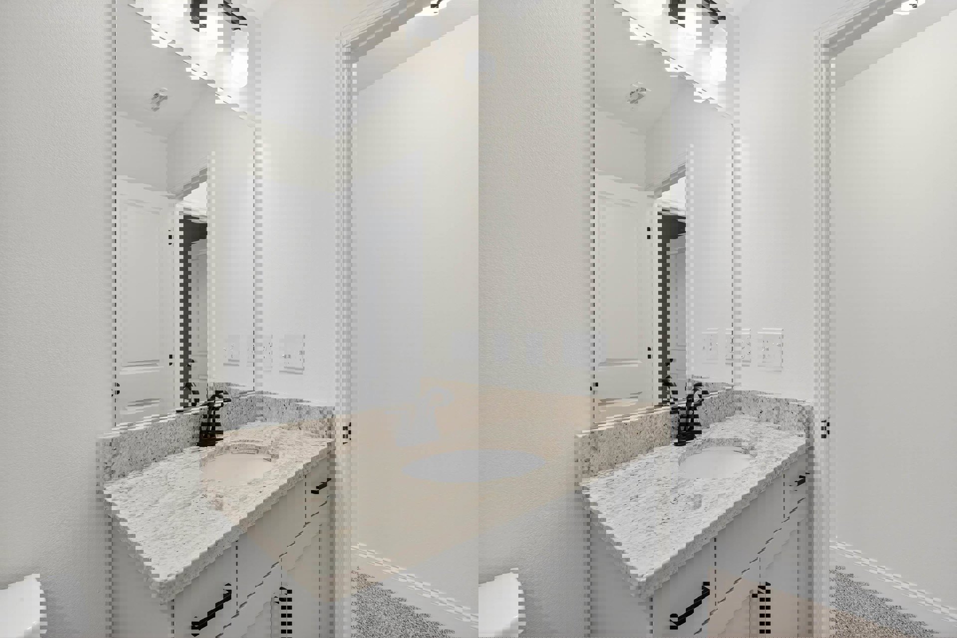 Bathroom with marble countertop, undermount sink, chrome faucet, large framed mirror, white cabinetry, white toilet, light switch panel, and white door with black handle
