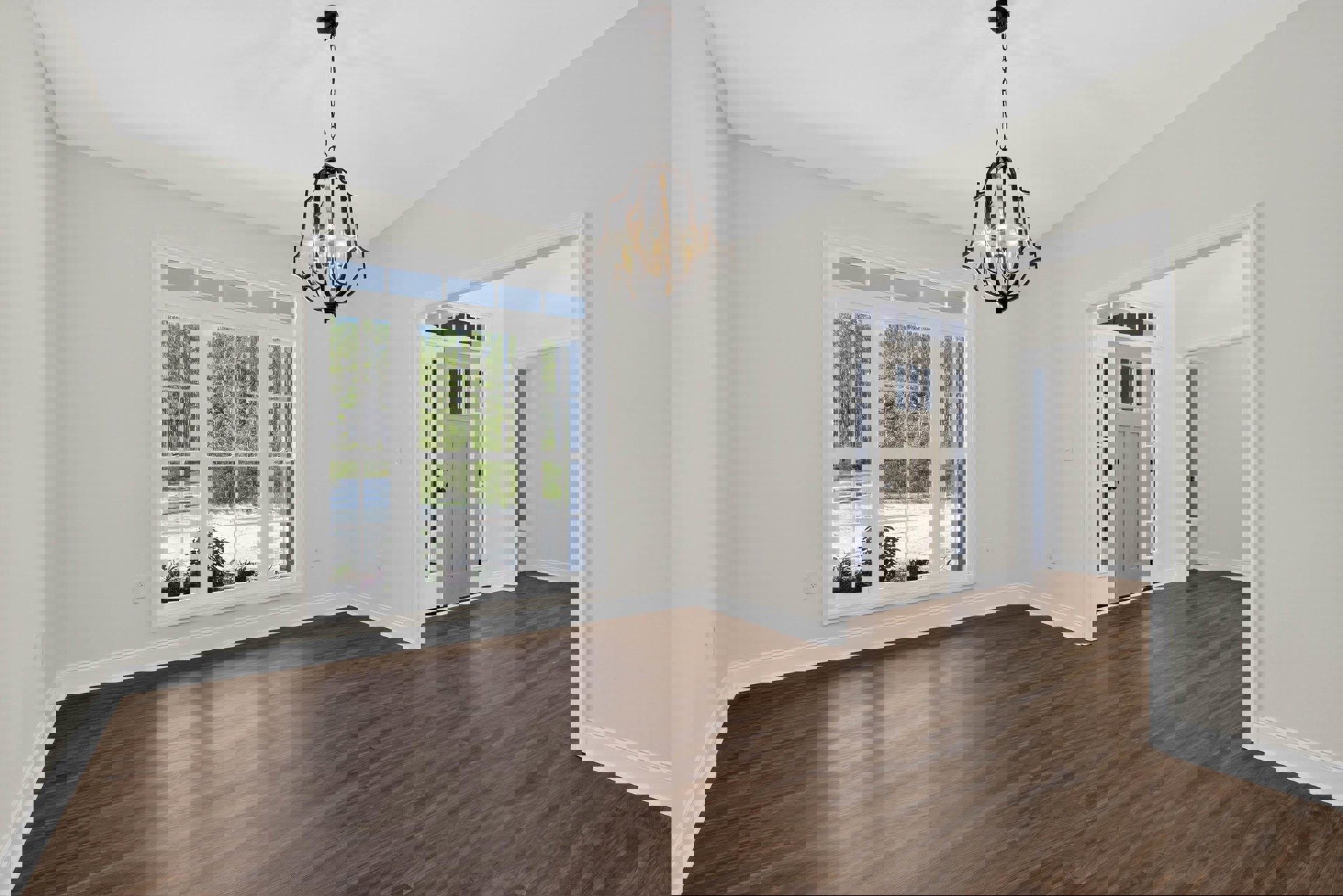 Chandelier hanging from ceiling above hardwood floor, large window with view of trees, white plaster walls with decorative molding, close-up of wooden door