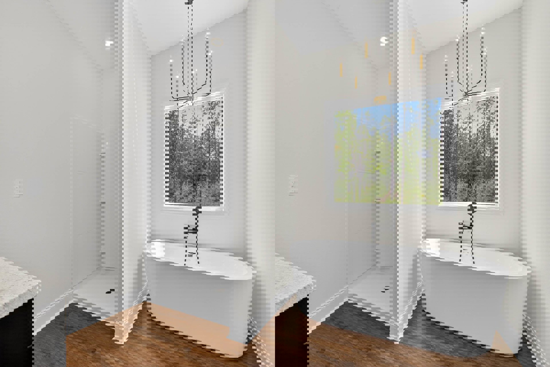 Bathroom featuring a white freestanding tub with black plumbing fixtures, glass-enclosed shower, tile flooring, window overlooking trees, white countertop, and modern light switch