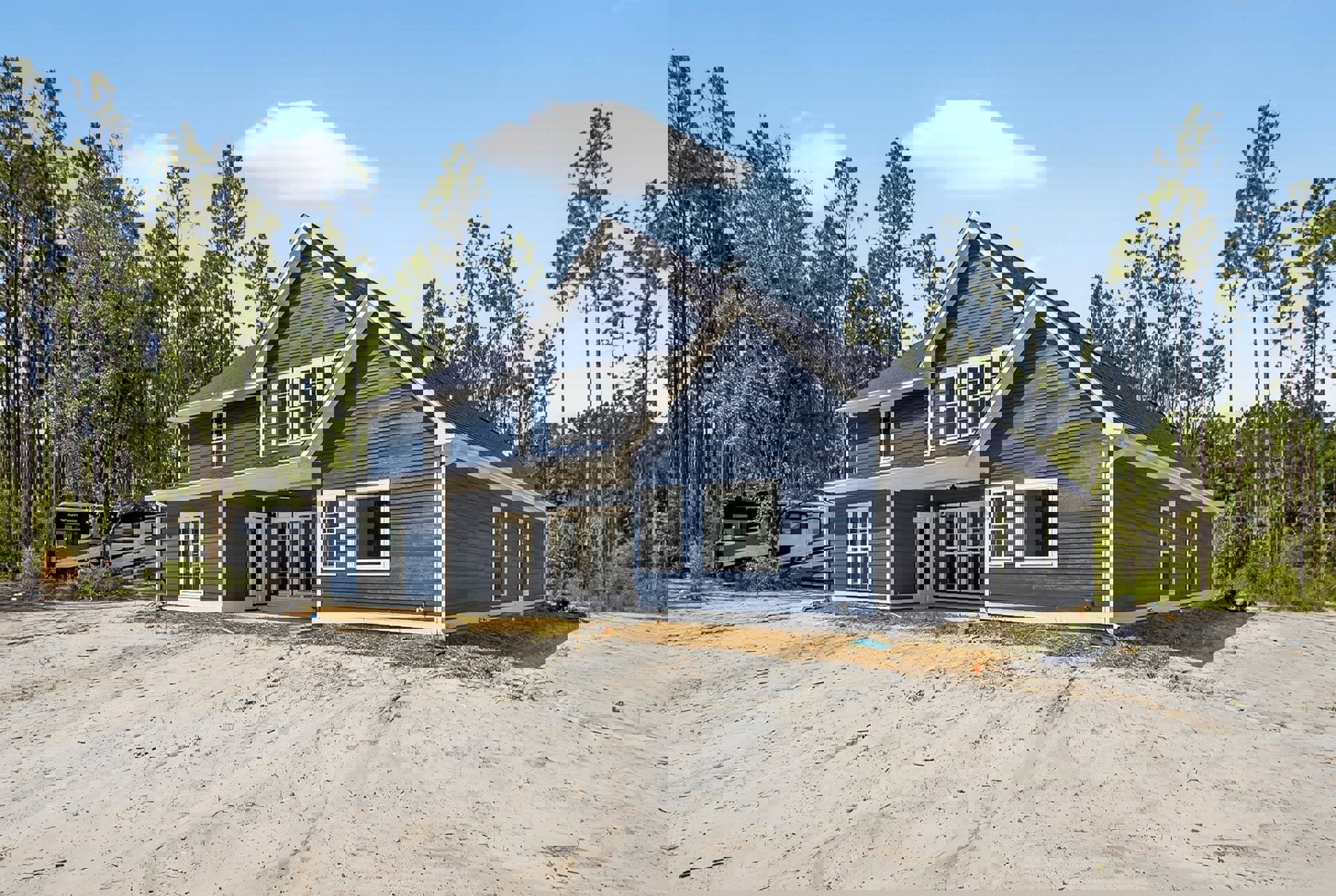 Blue house with white trim, blue siding, white-framed windows, trees in the background, cloudy sky, black and white van parked nearby