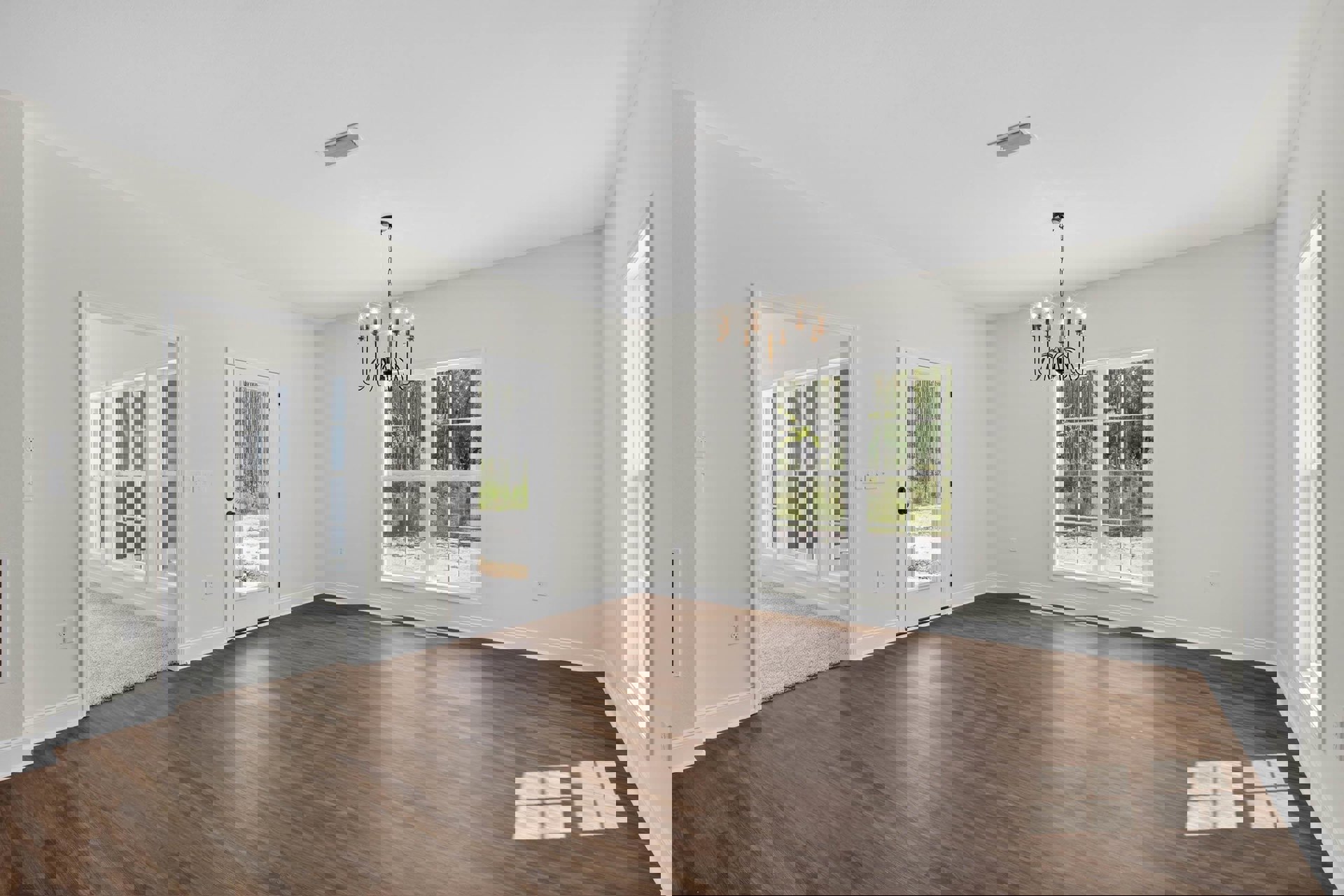 Chandelier hanging from ceiling above hardwood floor, white walls, large window and glass door offering forest views, brown surface with white square tiles