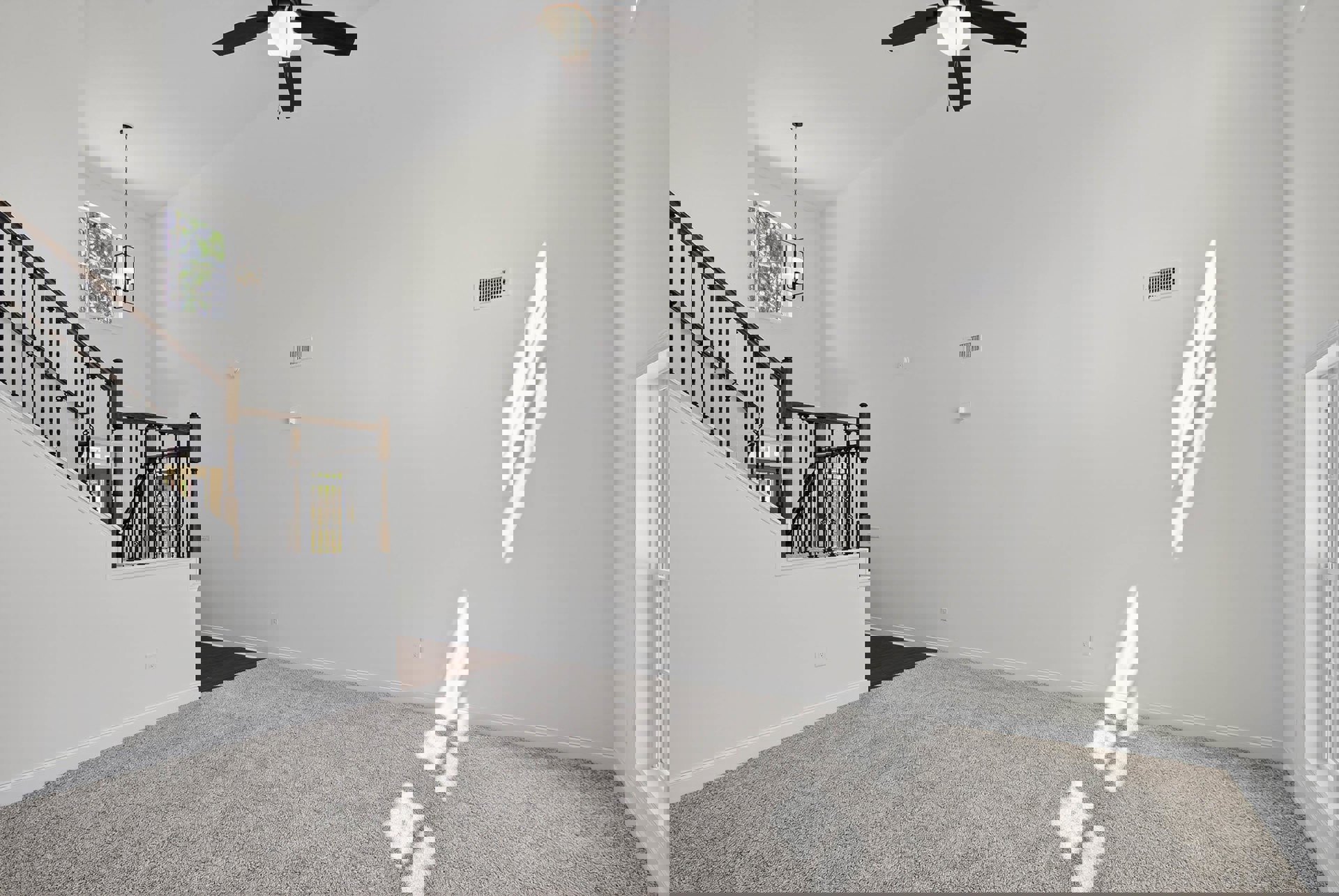 Carpeted room with ceiling fan and light, staircase with white railing, large window casting shadows, white doors, trees visible outside