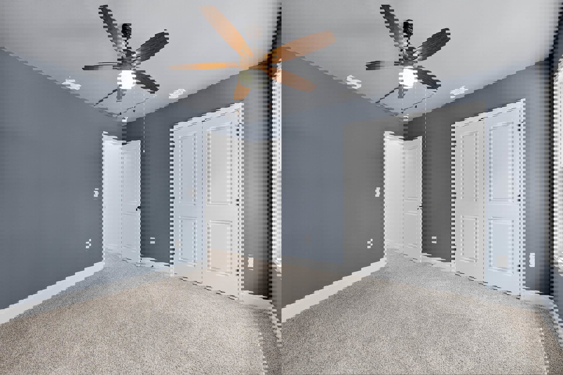 Carpeted room with white paneled doors featuring black handles and knobs, ceiling fan with integrated light, smooth plaster walls and ceiling