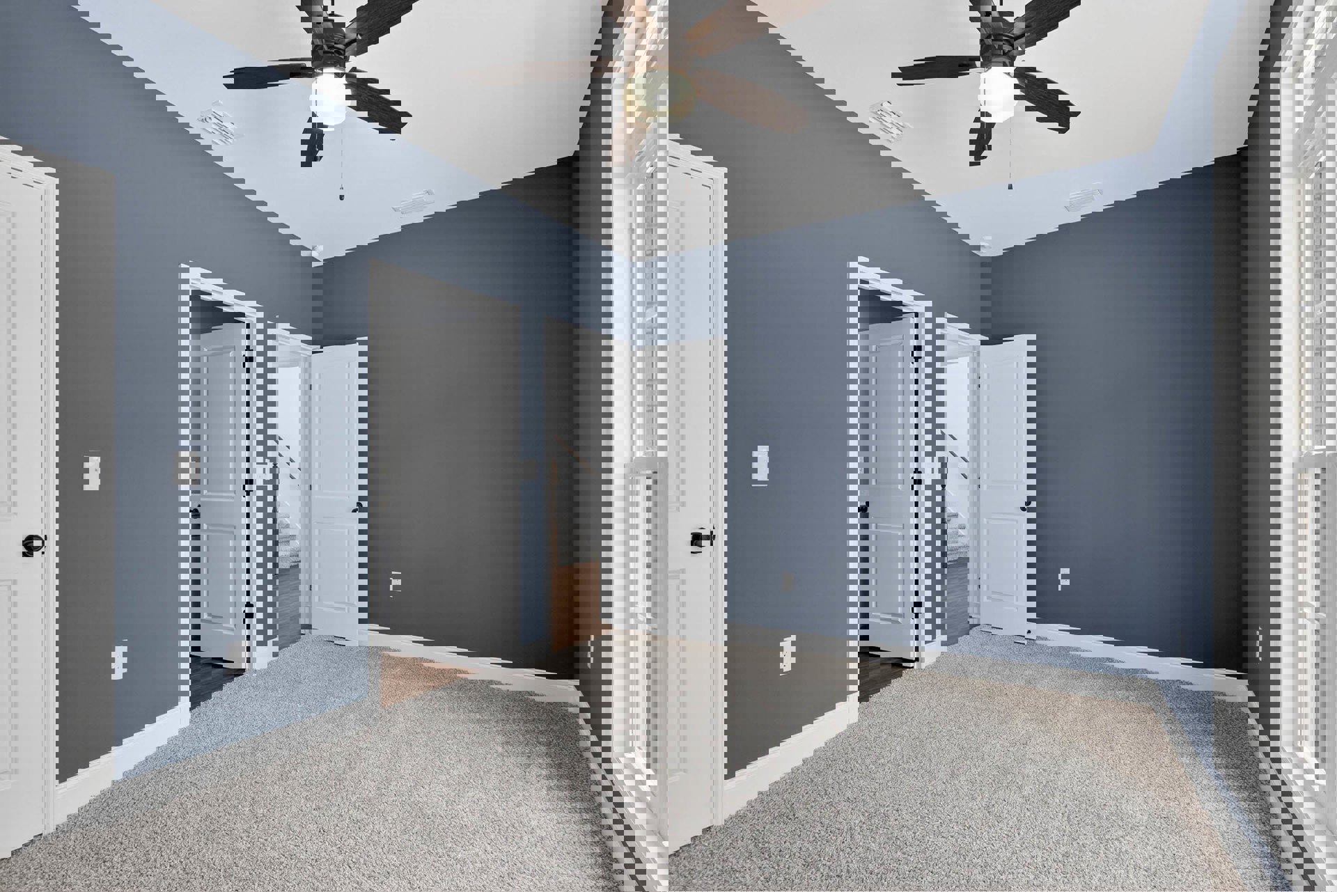 Blue-painted walls, white ceiling with a ceiling fan and light, white door with black knob, beige carpeted floor, white baseboards and crown molding