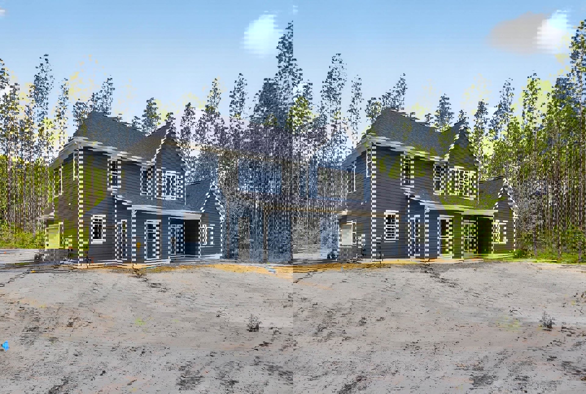 Blue house with white trim, paved driveway, and trees in the background; large window with white frame on the front facade.