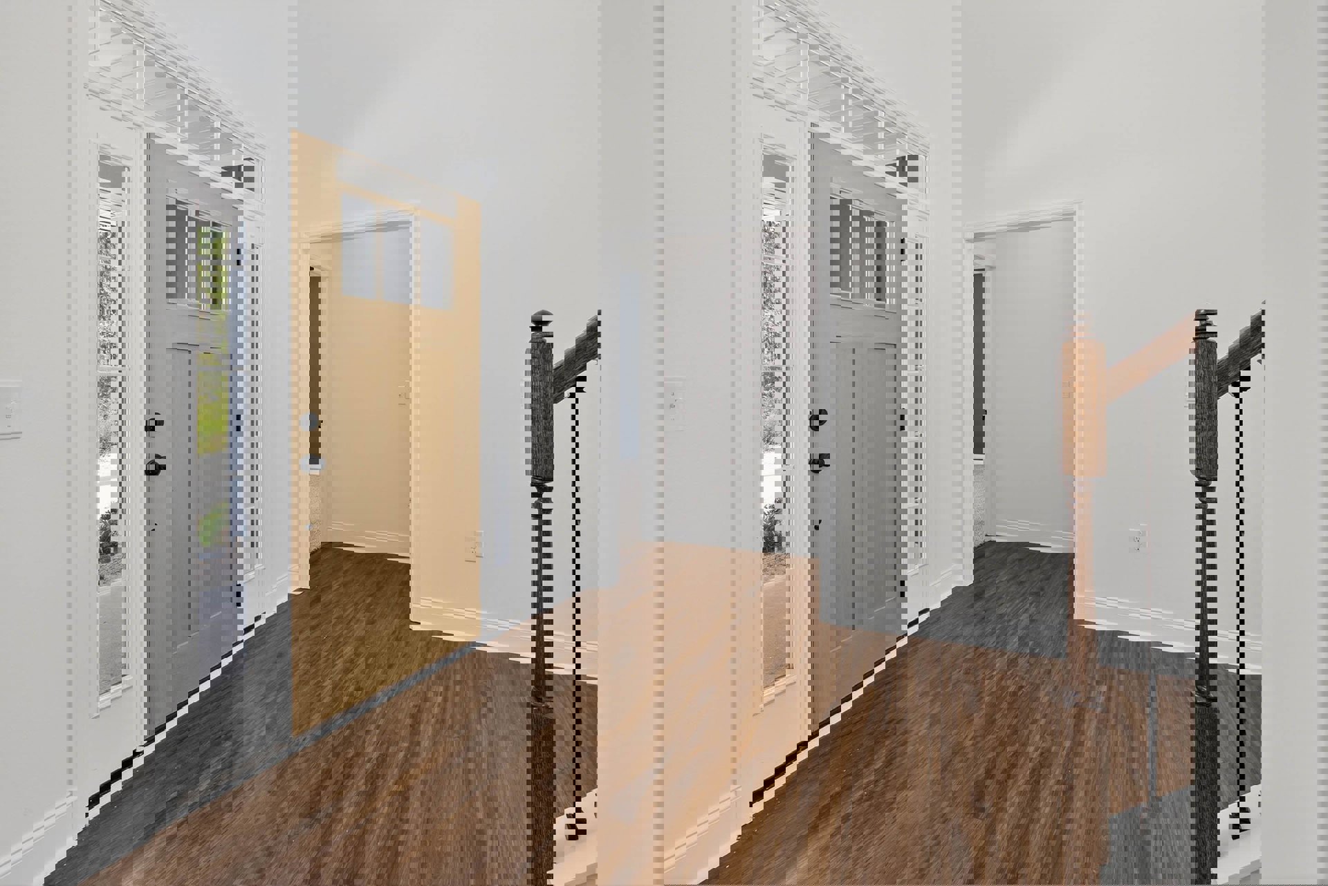 Room with hardwood flooring, white walls, wooden door with black handle, wood railing along hallway, light switch on wall