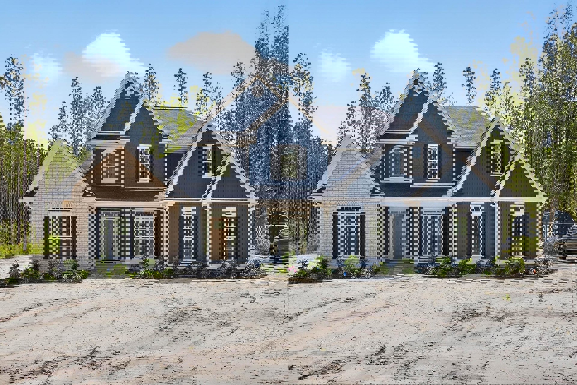 Blue and white house with glass-paneled white door, dirt patch in front, surrounded by tall trees in the background, partial view of a car near the entrance