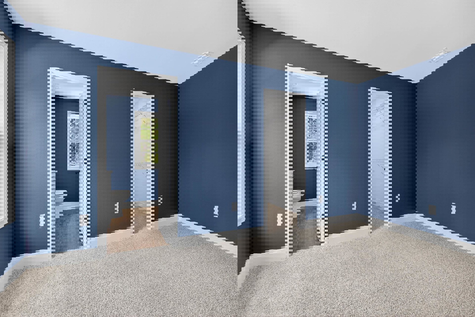 Bedroom with blue painted walls, light carpet flooring, open door revealing closet, white-framed window, adjacent bathroom featuring window and toilet