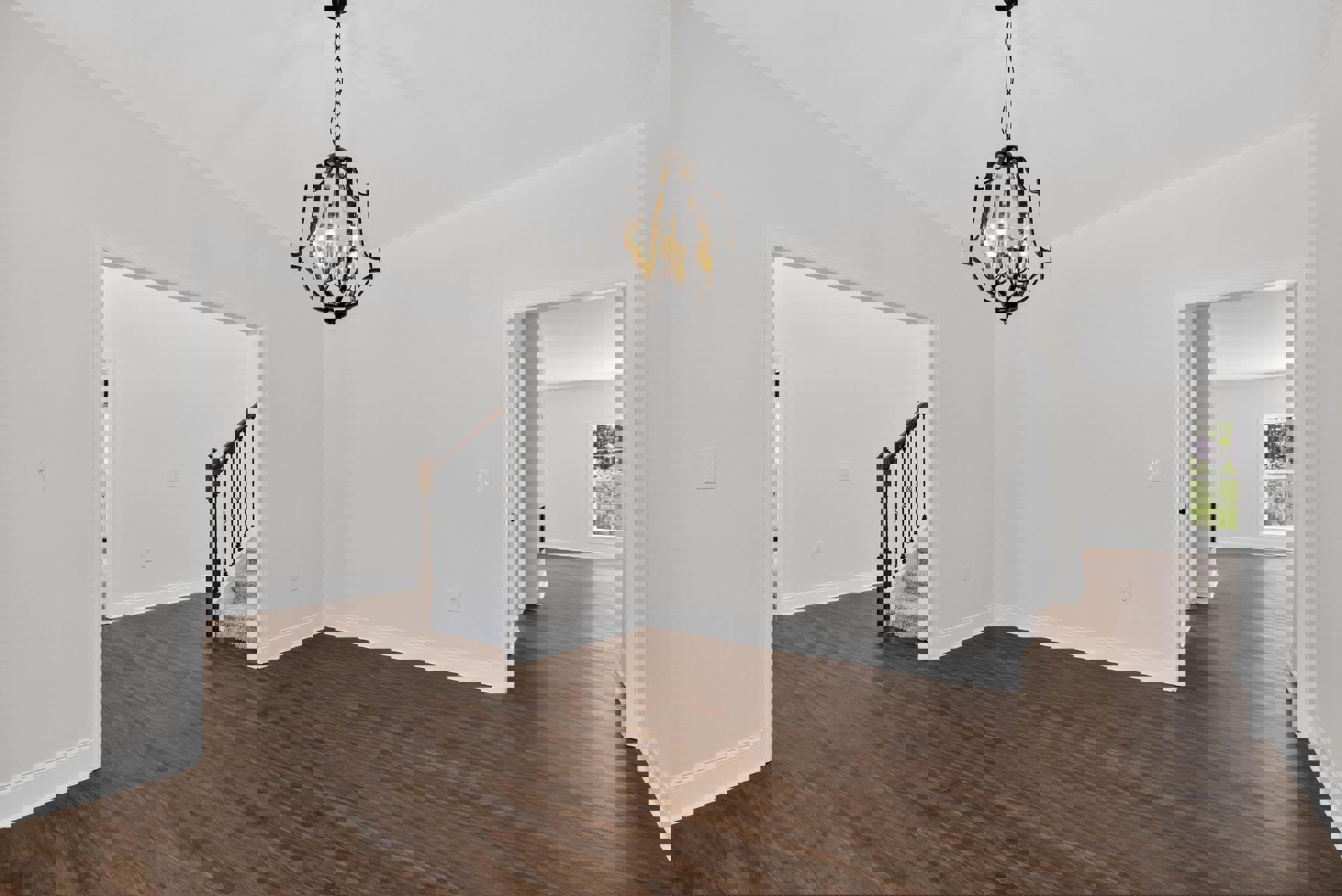 Chandelier with crystal accents hanging from white ceiling, hardwood flooring, staircase with dark wood railing, large window overlooking green trees, neutral plaster walls