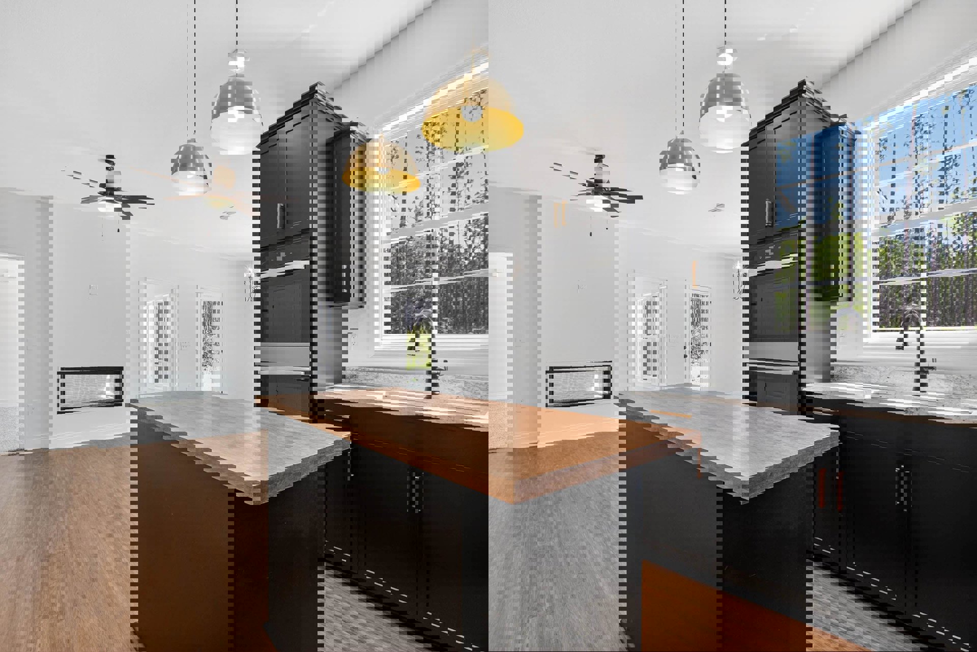 Kitchen with wood island, black base countertop, ceiling fan with light, large window showing trees, cabinetry and drawers, modern light fixture, stainless steel sink