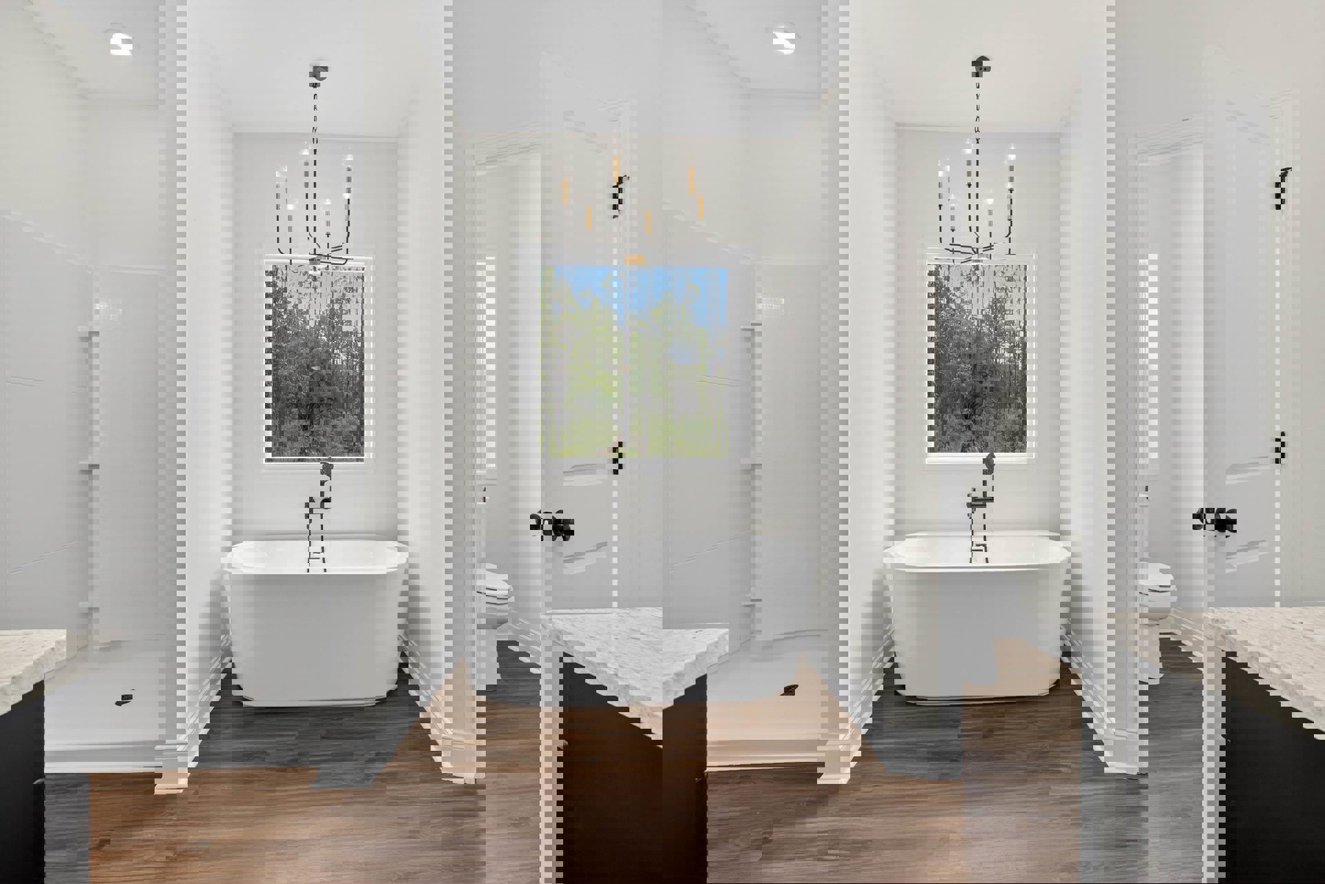 Bathroom with freestanding white tub, modern toilet, light tile flooring, large window showing trees, and stone countertop with chrome faucet.