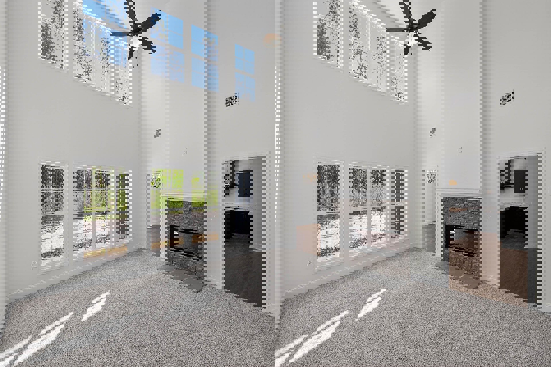 Living room with beige carpet, stone fireplace, ceiling fan with light, built-in cabinetry, and large window letting in natural light