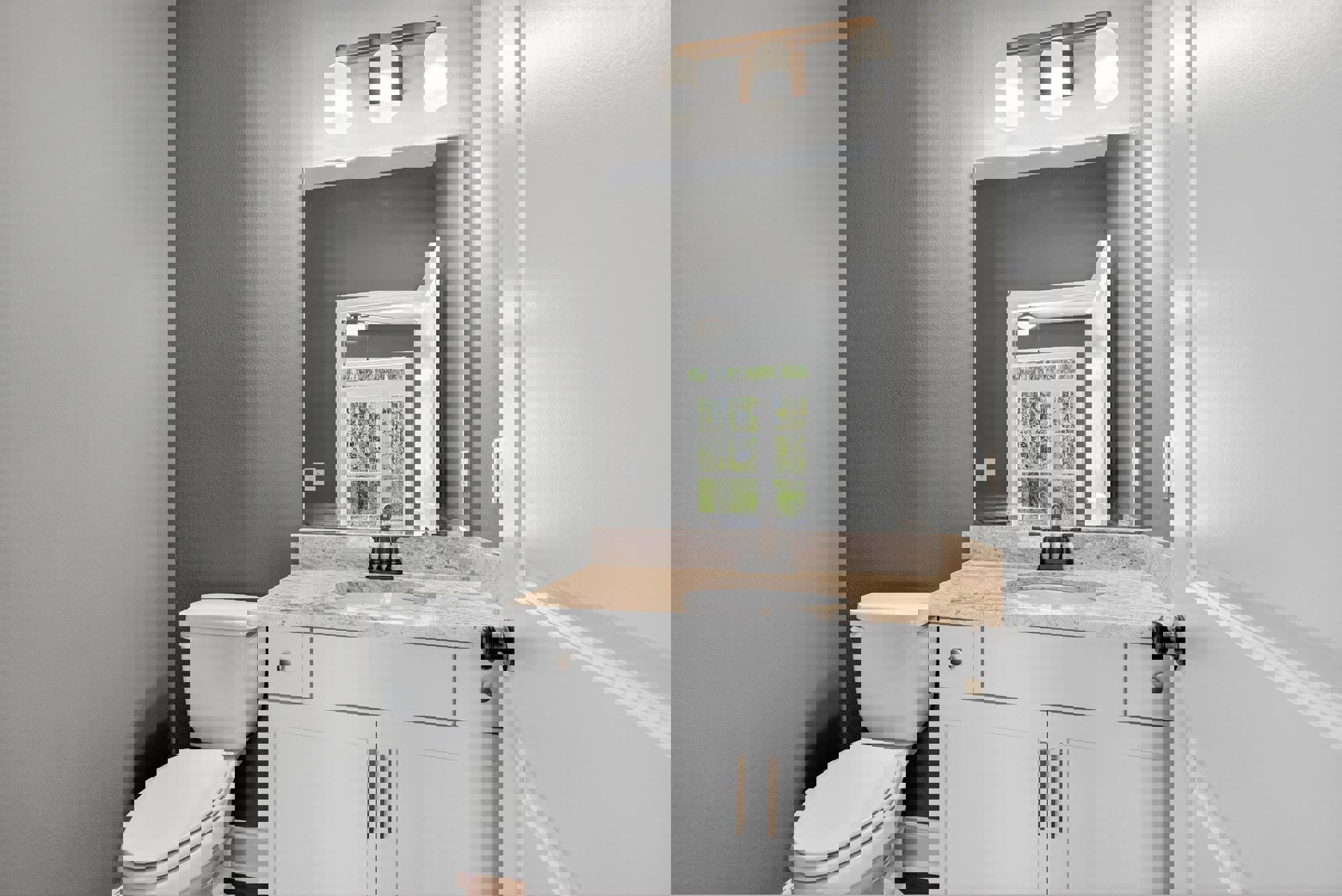 Modern bathroom with white porcelain sink, wall-mounted mirror, white toilet, tiled walls, and window overlooking trees