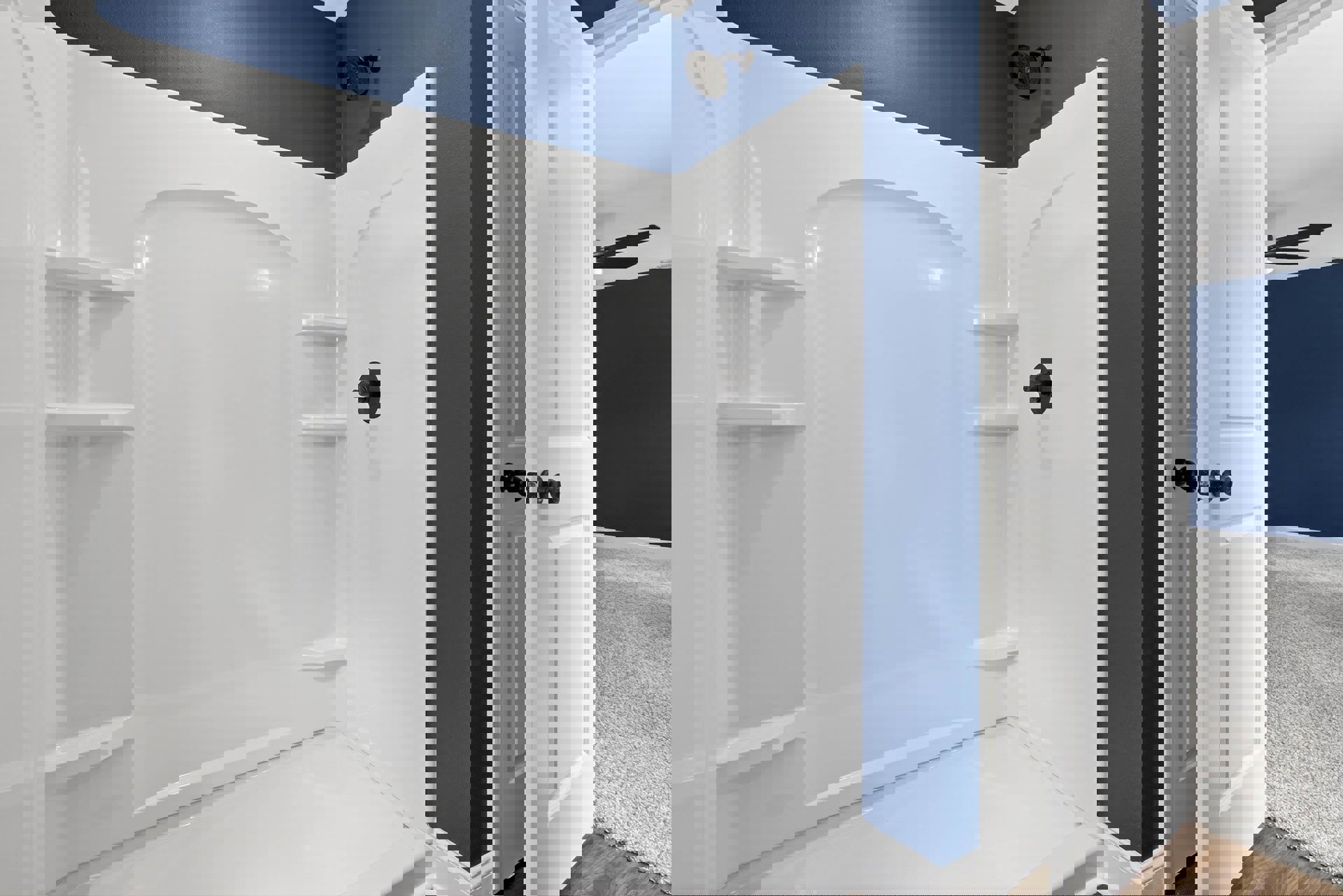 White tile shower with built-in shelves, blue accent wall, chrome shower head, and white bathroom finishes