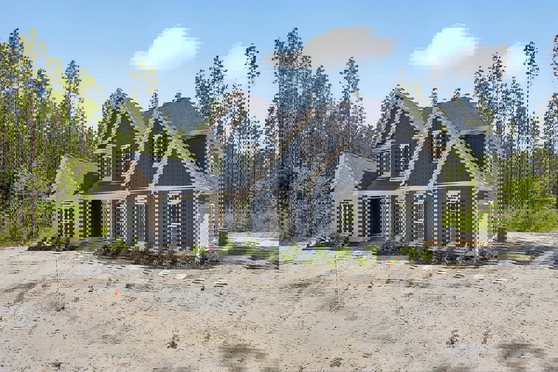 Blue metal roof house surrounded by bare dirt and mature trees, white framed windows, grey rectangular utility box on ground, dirt driveway, partly cloudy sky