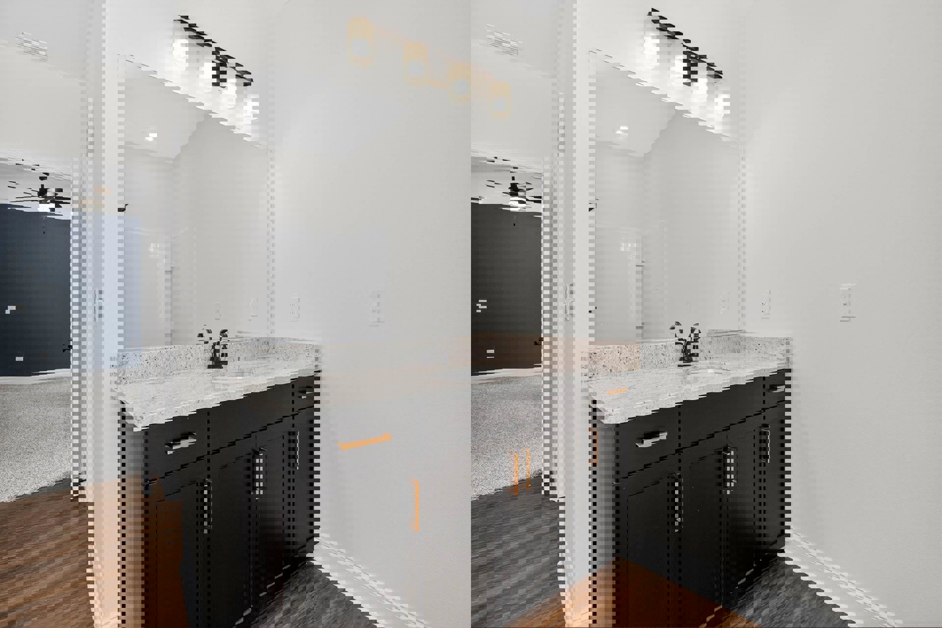 Bathroom with dark blue accent wall, black and gold vanity, white countertop sink, rectangular mirror, ceiling row of lights, and black door.