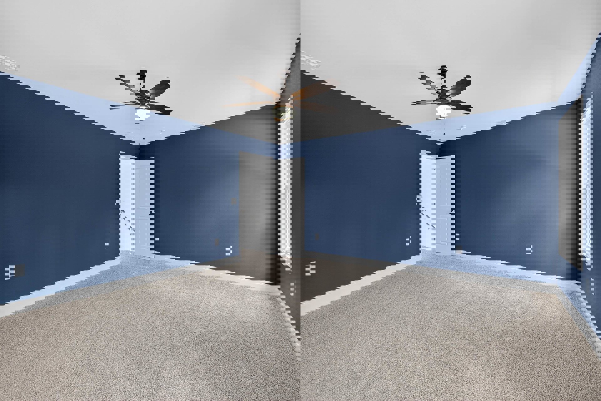 Ceiling fan with light fixture, blue painted walls, white door with black knob, white window frame, carpeted floor, open door with handrail