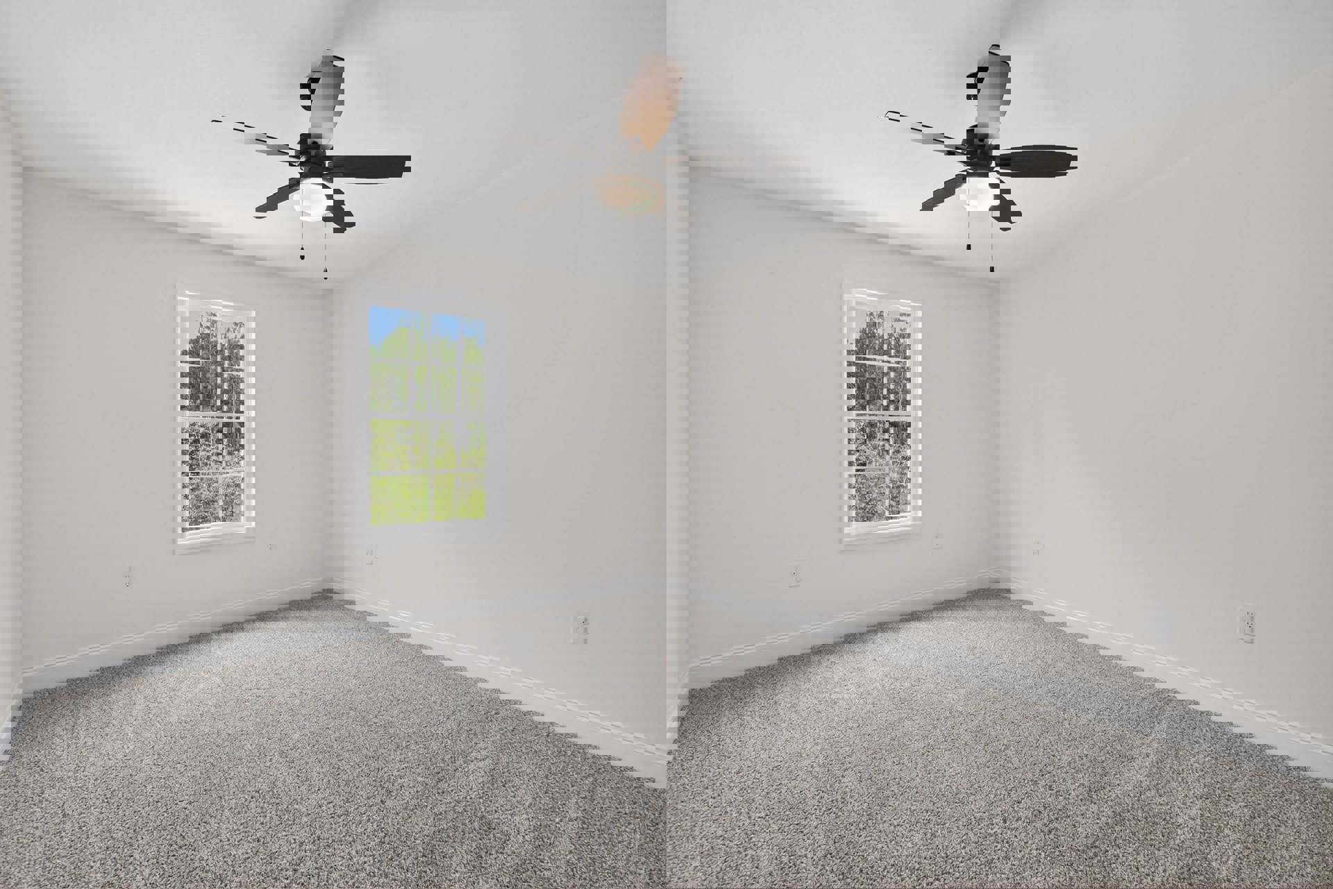 Neutral-toned carpeted room with white walls, ceiling fan with light fixture, large window showing leafy trees outside