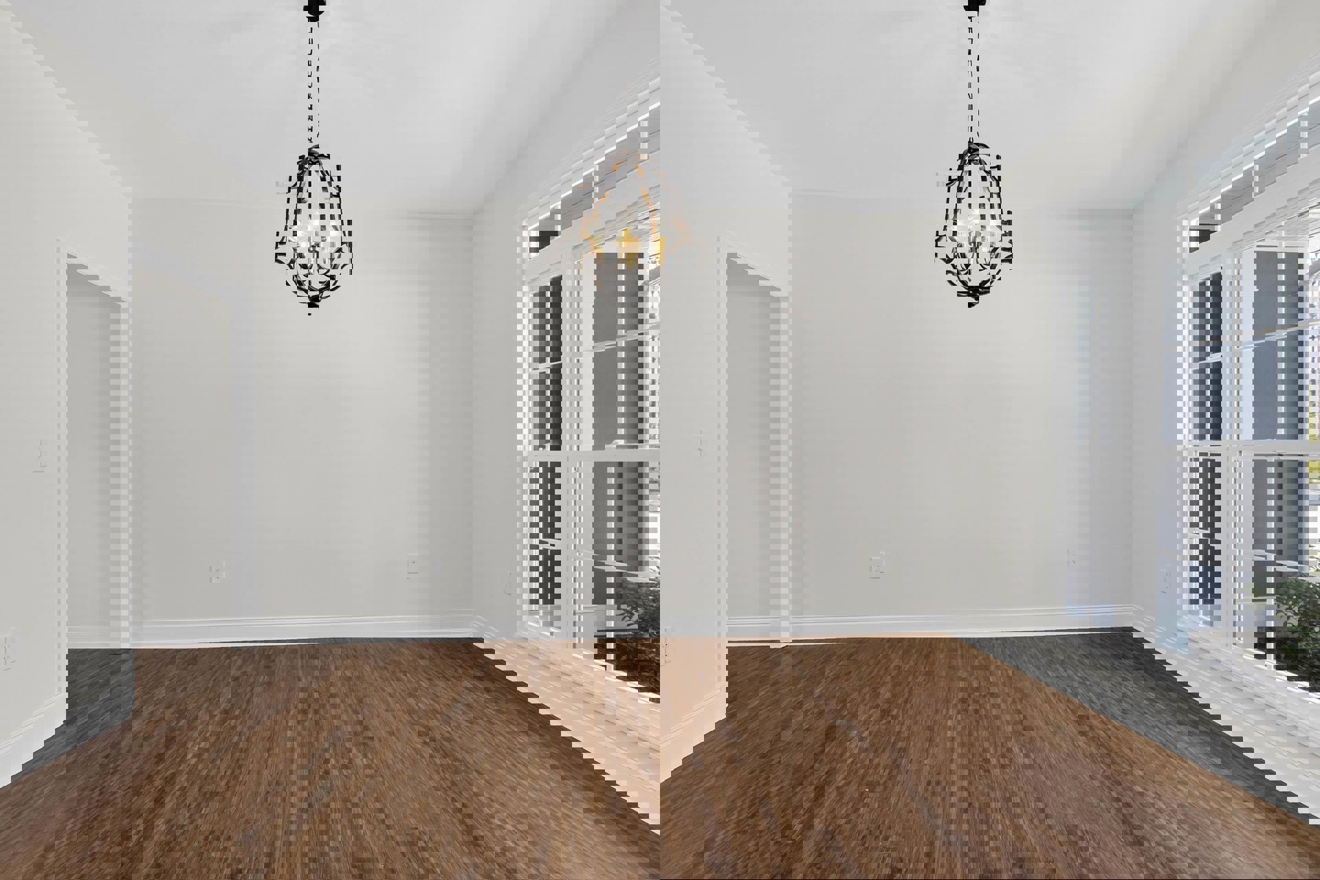 Chandelier with crystal accents hanging from ceiling, hardwood floor with white baseboard trim, white framed window, and white paneled door in a spacious room