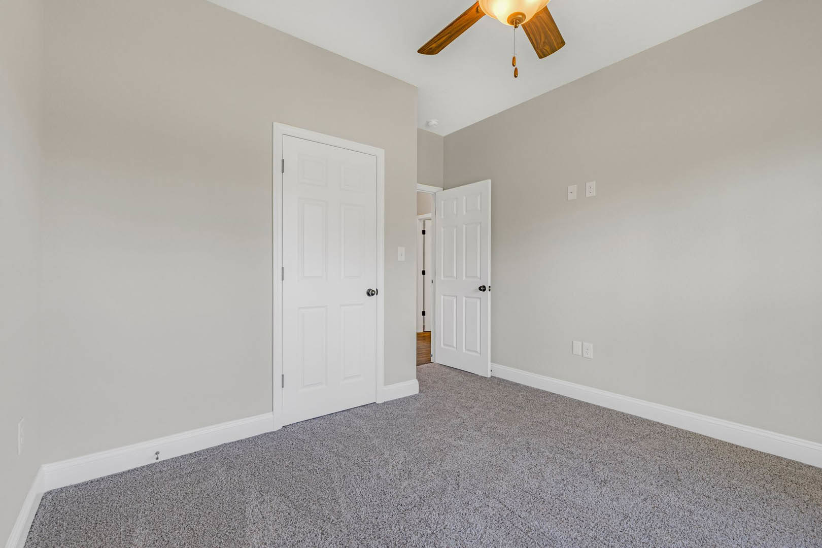 Carpeted room with white doors featuring silver and black handles, white trim, ceiling fan, and exposed wooden ceiling beam