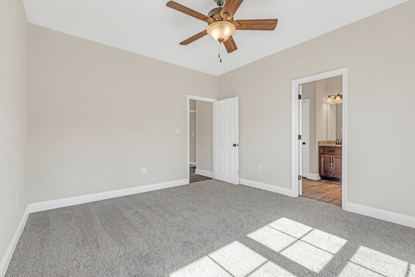 Ceiling fan with light fixture, white door with black knob, wooden cabinet, carpet over hardwood floor, white walls with crown molding