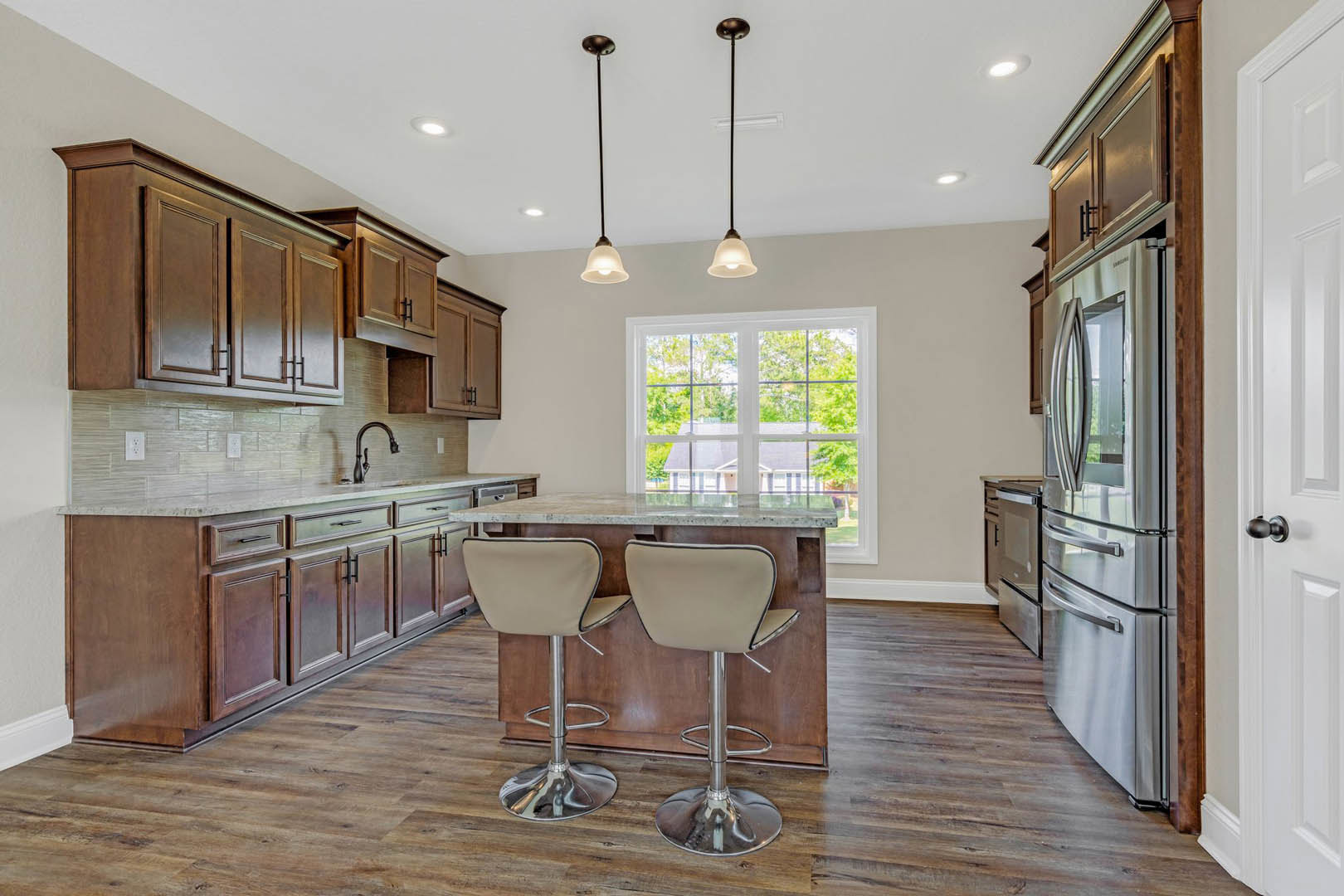 Open-concept kitchen featuring a bar with upholstered stools, stainless steel refrigerator, white cabinetry, stone countertops, modern faucet, and large windows providing natural