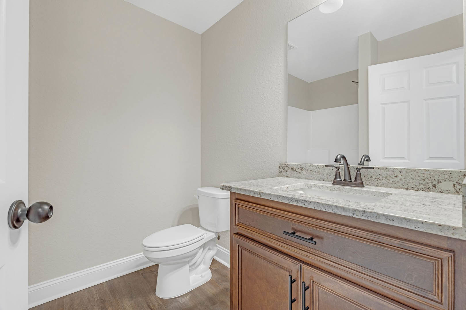 Bathroom with white toilet and pedestal sink, tiled floor, white door with metal handle, chrome towel bar, and neutral wall finishes