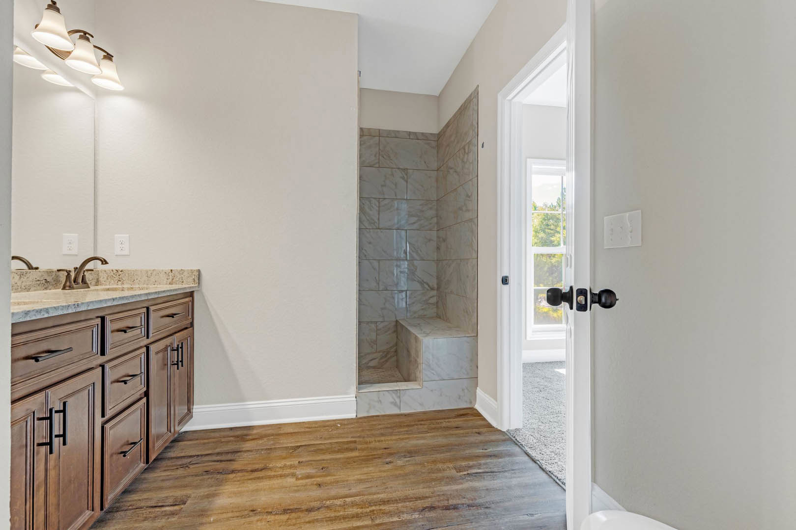 Bathroom with glass-enclosed shower, white sink on wood vanity, wood flooring with white baseboards, tiled wall detail, brushed metal door knob, modern multi-bulb light fixture