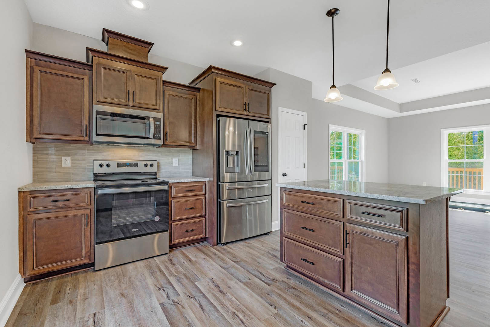 Kitchen with natural wood cabinets, stainless steel refrigerator and oven, built-in microwave, white-framed window, and light countertops