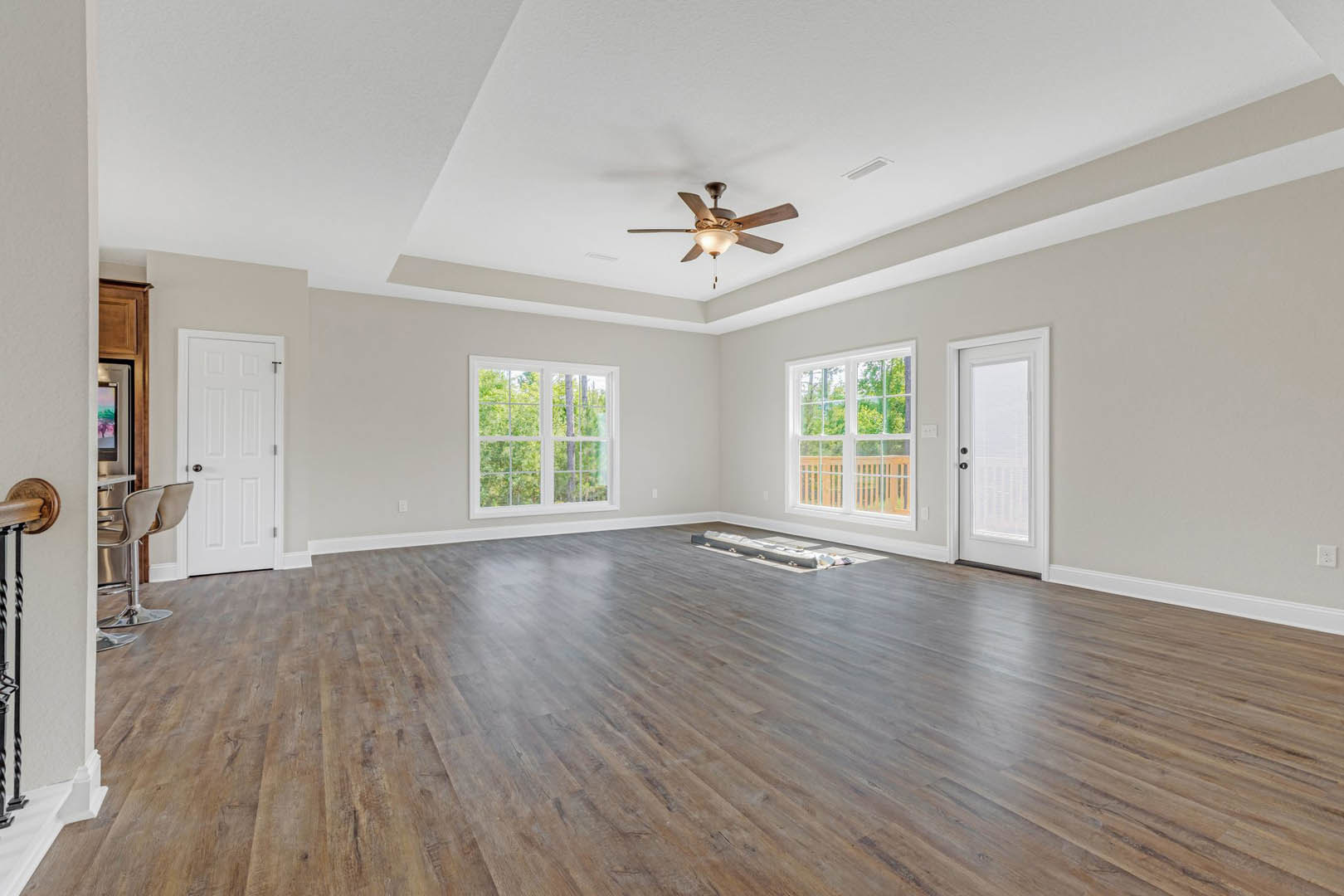Hardwood floor room with ceiling fan, white walls, large windows showing trees and deck, white door with silver handle