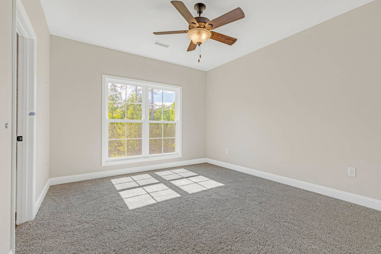 Bedroom with white carpet, ceiling fan with light fixture, large window overlooking trees, neutral walls with crown molding