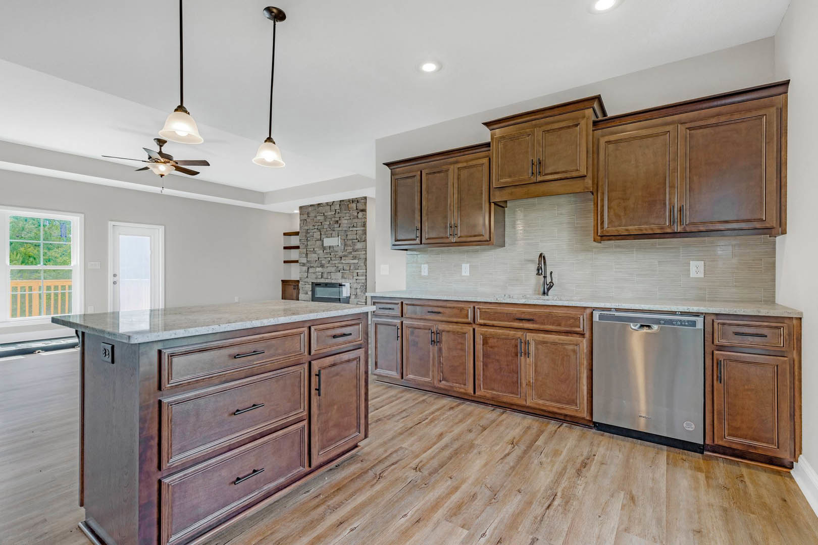 Kitchen with natural wood cabinets, stainless steel dishwasher, white-framed window, light stone countertop, and drawers.