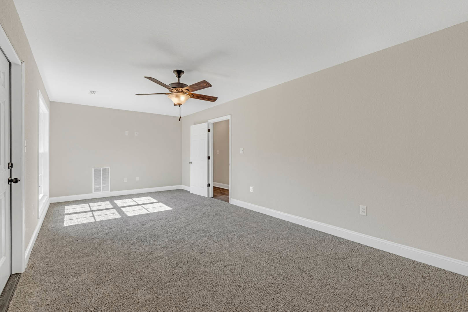 Bedroom with white carpet, ceiling fan with light, white door and light switch, window with white blinds, pale walls and baseboard molding