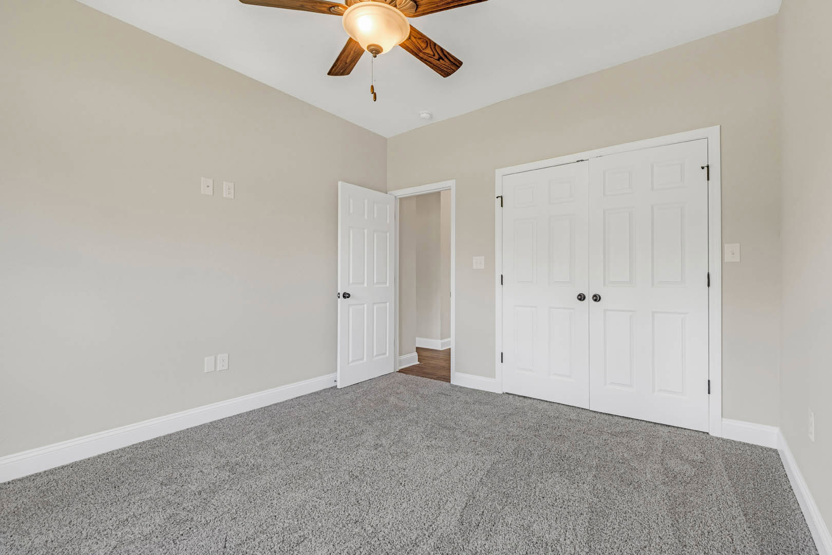 Carpeted room with white walls, ceiling fan with light, white double doors featuring black knobs, and door frame molding.