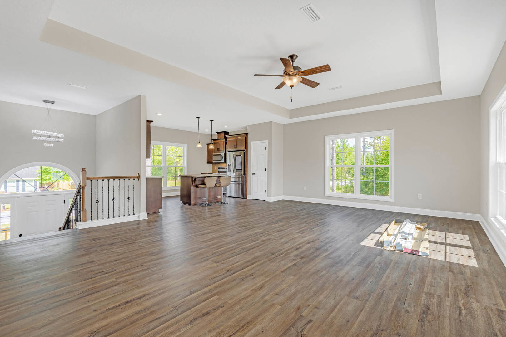 Hardwood floor room with ceiling fan, window showing trees outside, chair beside table, and close-up of wooden railing