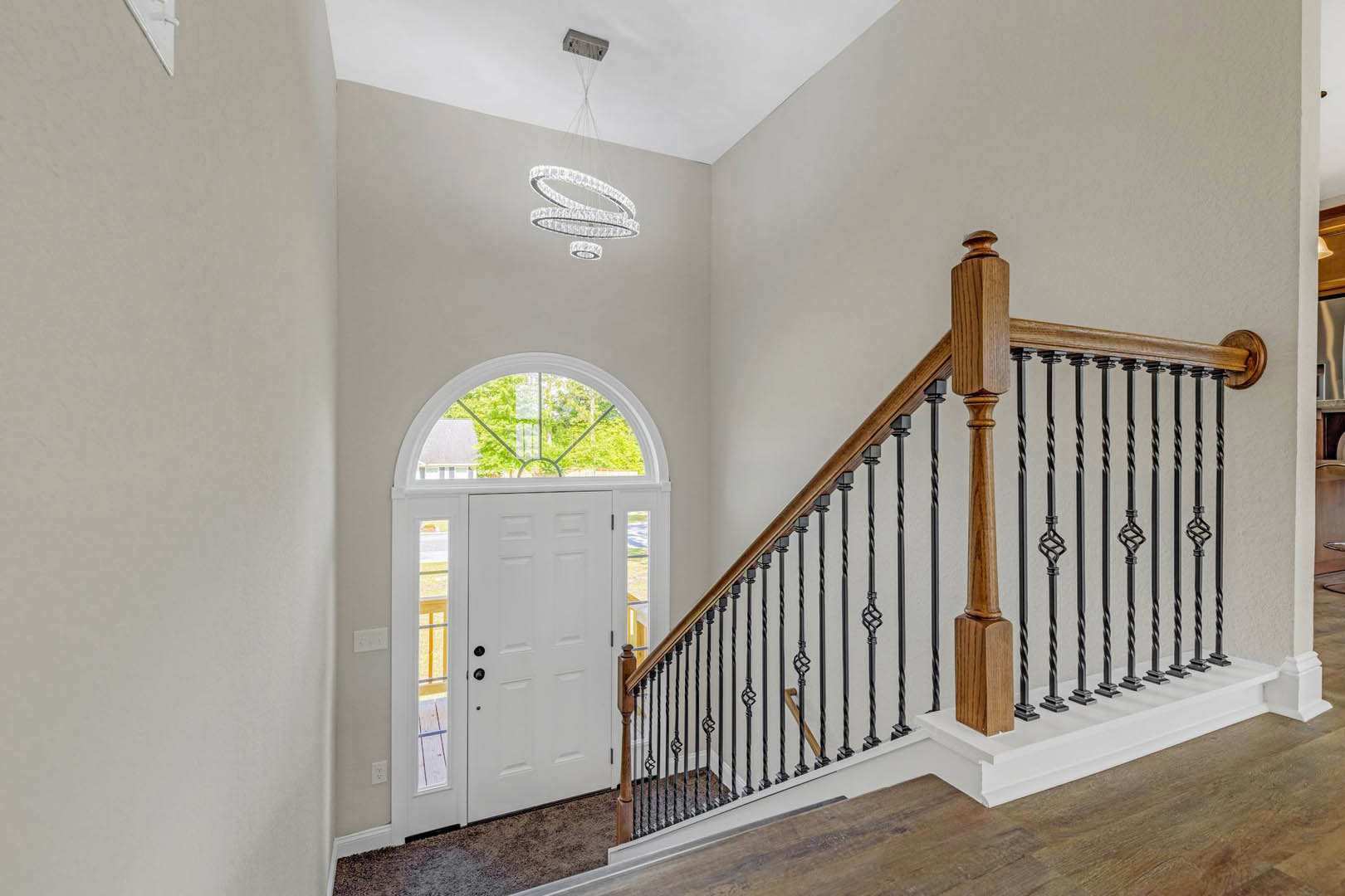 Wood staircase with matching railings and balusters, hardwood floor, white door with glass window, chandelier overhead, white-framed window, crown molding along ceiling.