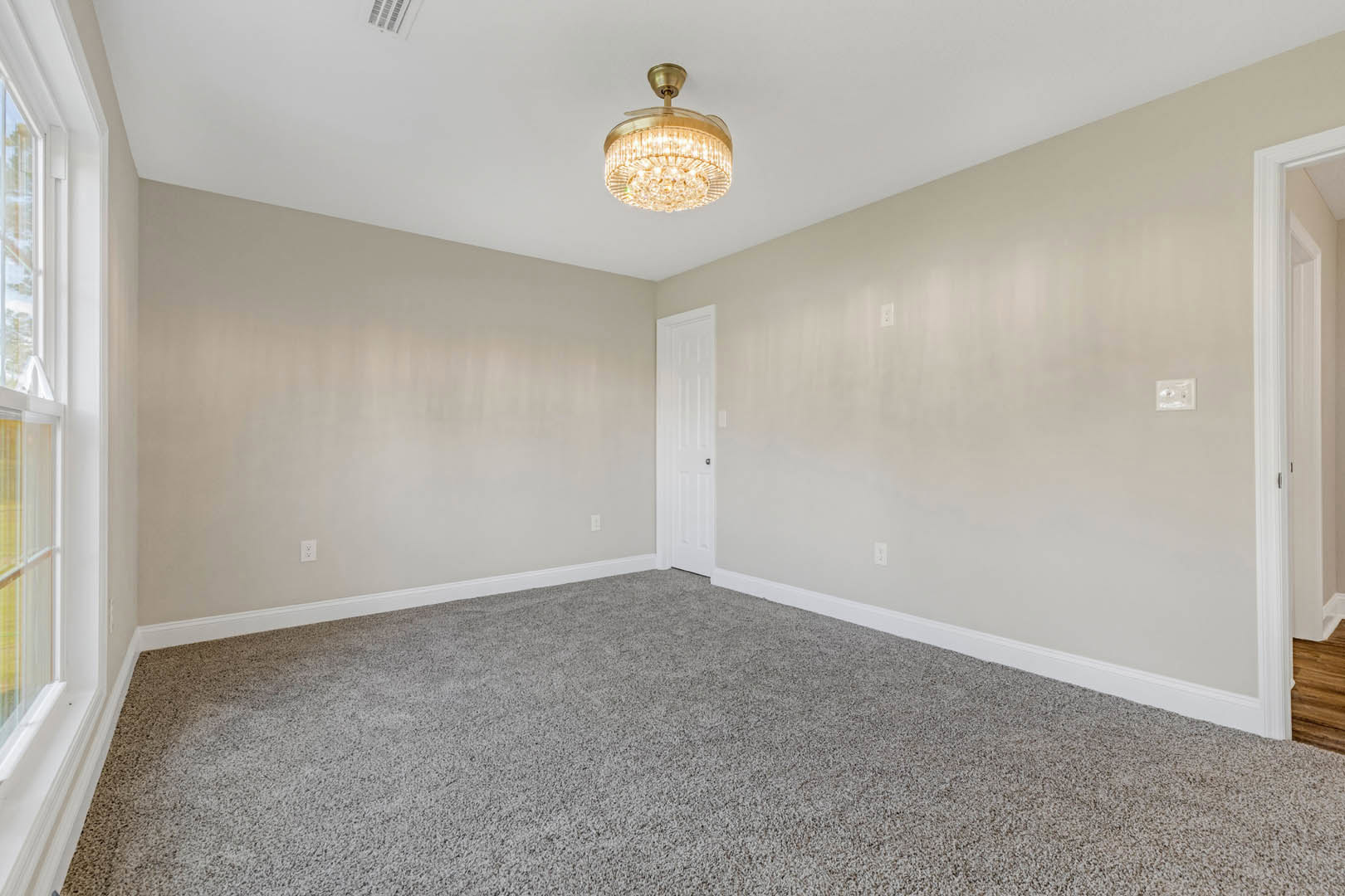 Carpeted room with white walls, decorative chandelier, white door with black handle, and white light switch; ceiling features crown molding.