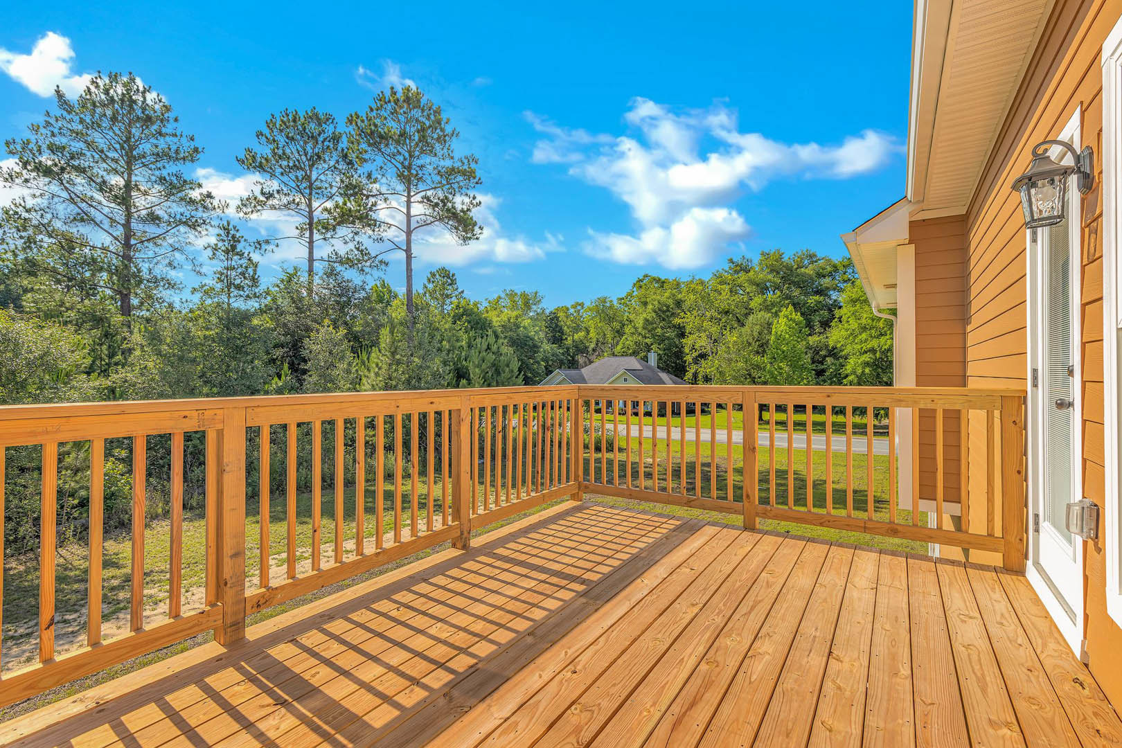 Wooden deck with railing, white exterior door, fenced perimeter, group of trees, blue sky with clouds