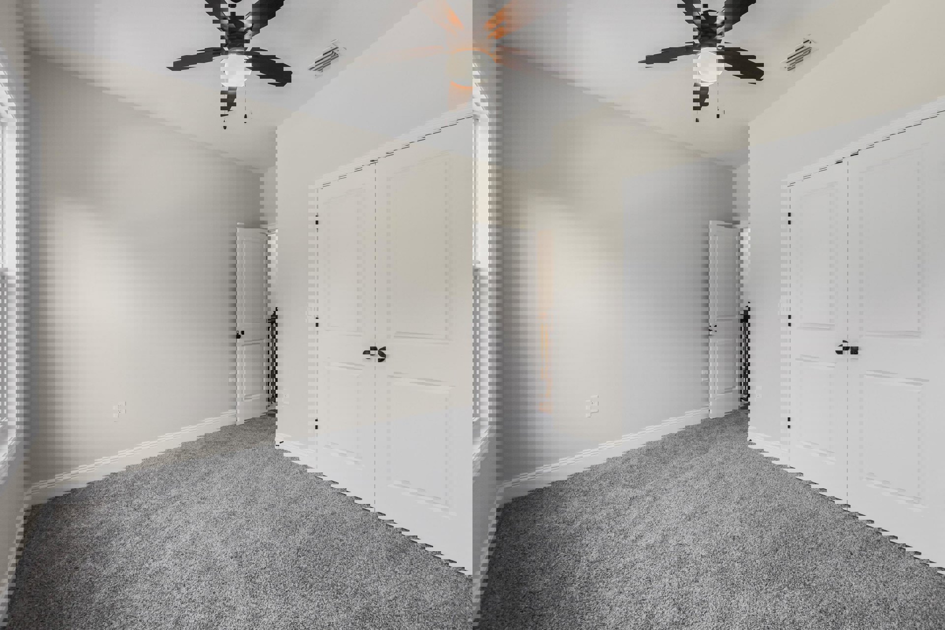 Ceiling fan with light fixture mounted on white plaster ceiling, two white doors with black knobs, wood flooring, neutral walls