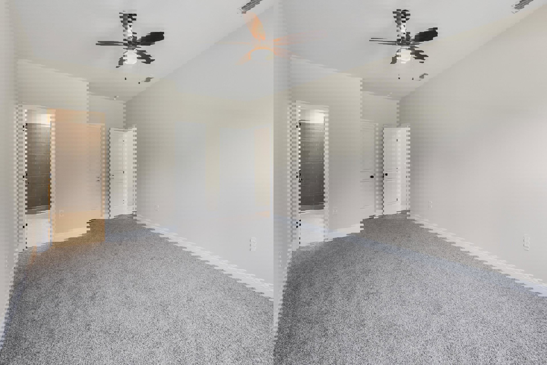 Carpeted room with white walls, ceiling fan with light fixture, white door featuring black knobs, partial view of tiled wall near doorway