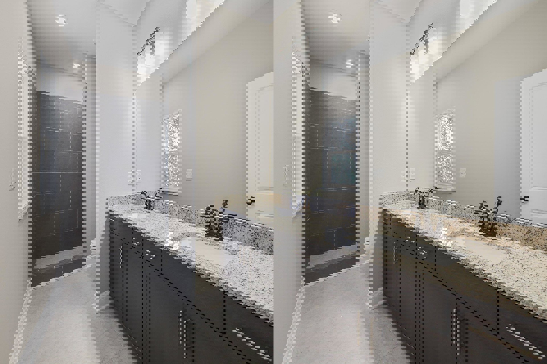 Double vanity bathroom with granite countertops, undermount sinks, chrome faucets, white cabinetry, grey tile backsplash, and window with white trim.