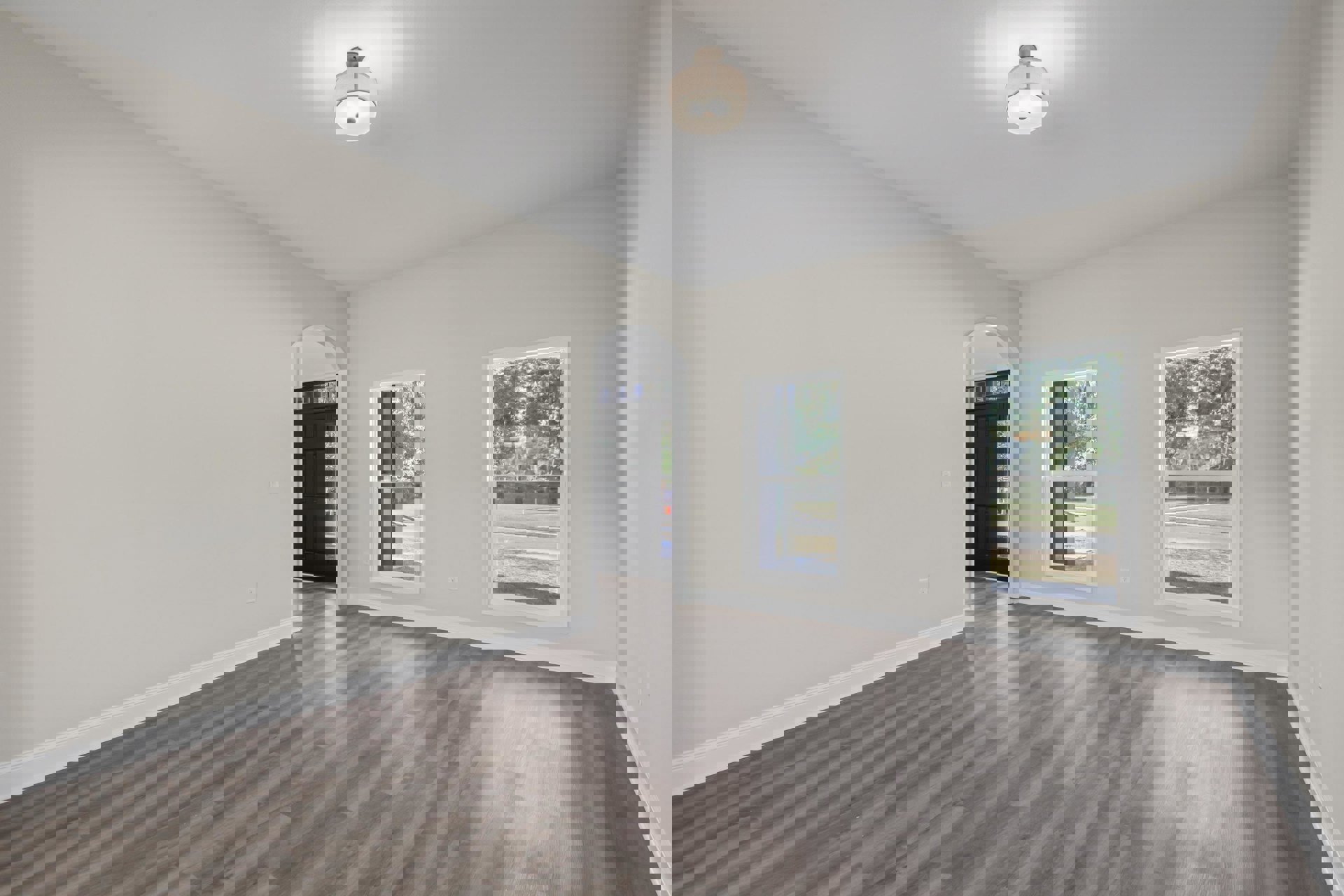 Room with wood flooring, black door with glass window, white-shaded ceiling light fixture, two windows showing street and trees, white plaster walls with crown molding.