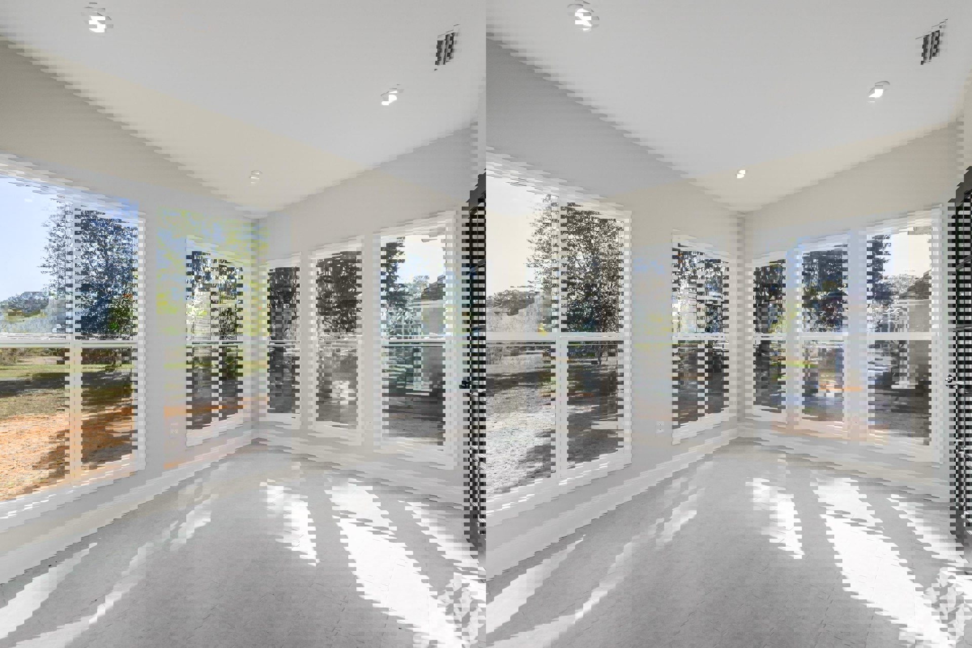 Spacious room featuring multiple large windows with white frames, white tile flooring, and a glass-paneled door; natural daylight fills the space, highlighting clean finishes and