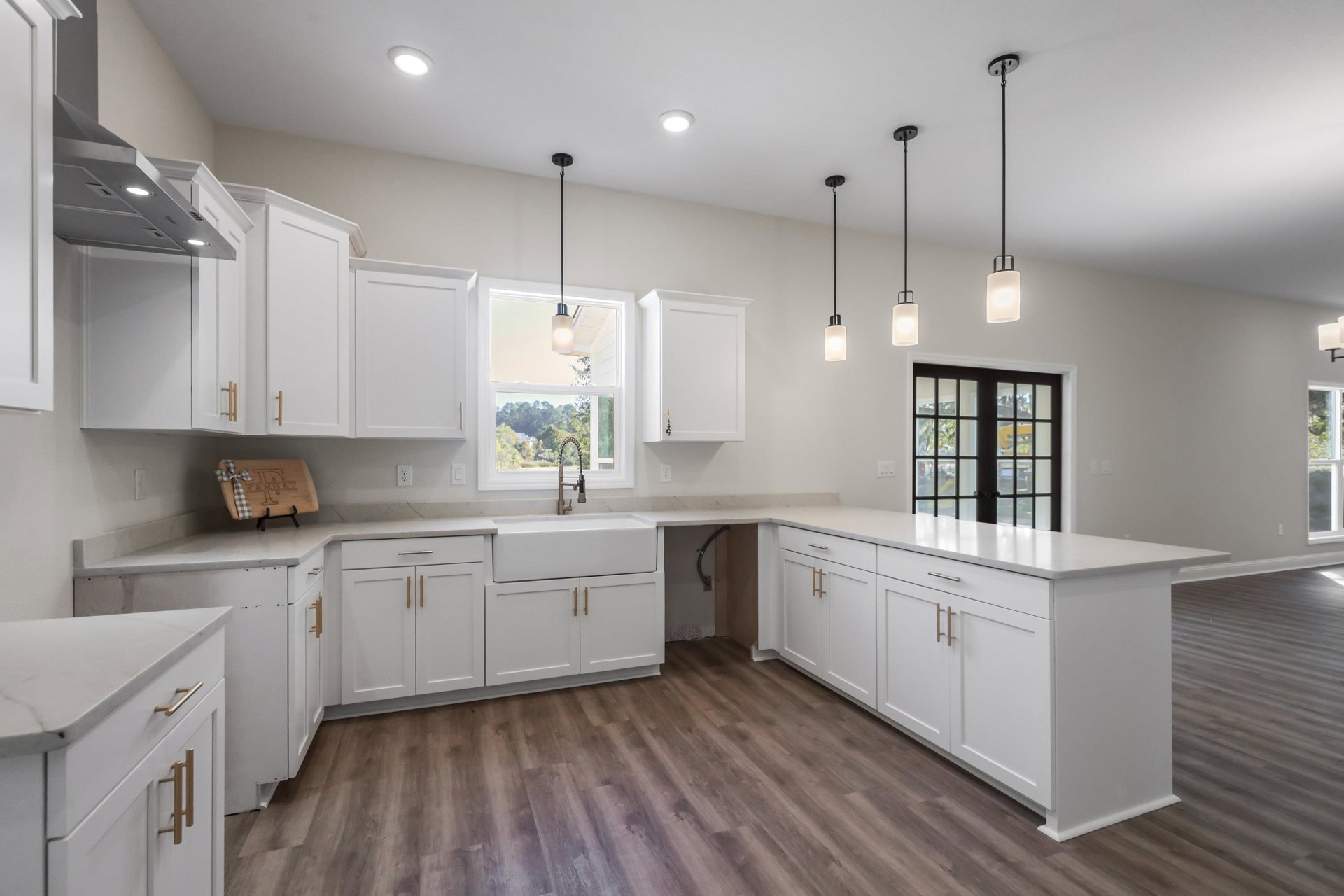 Kitchen with white shaker cabinets, wood plank flooring, white quartz countertops, stainless steel sink, and modern light fixture with white shade