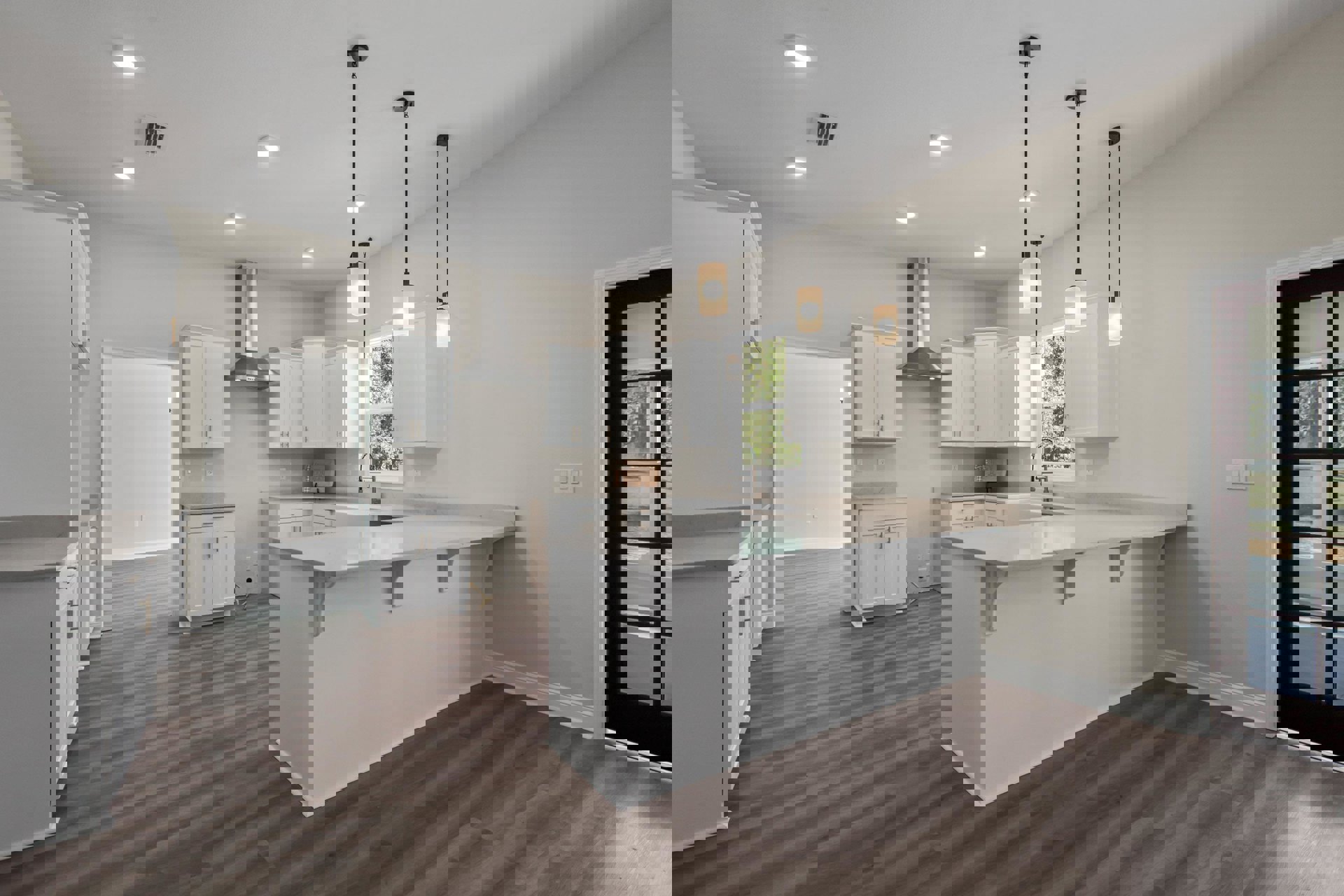 White kitchen cabinets with brushed metal handles, wood plank flooring, stone countertop, stainless steel sink, large window overlooking grassy yard, recessed ceiling lights.