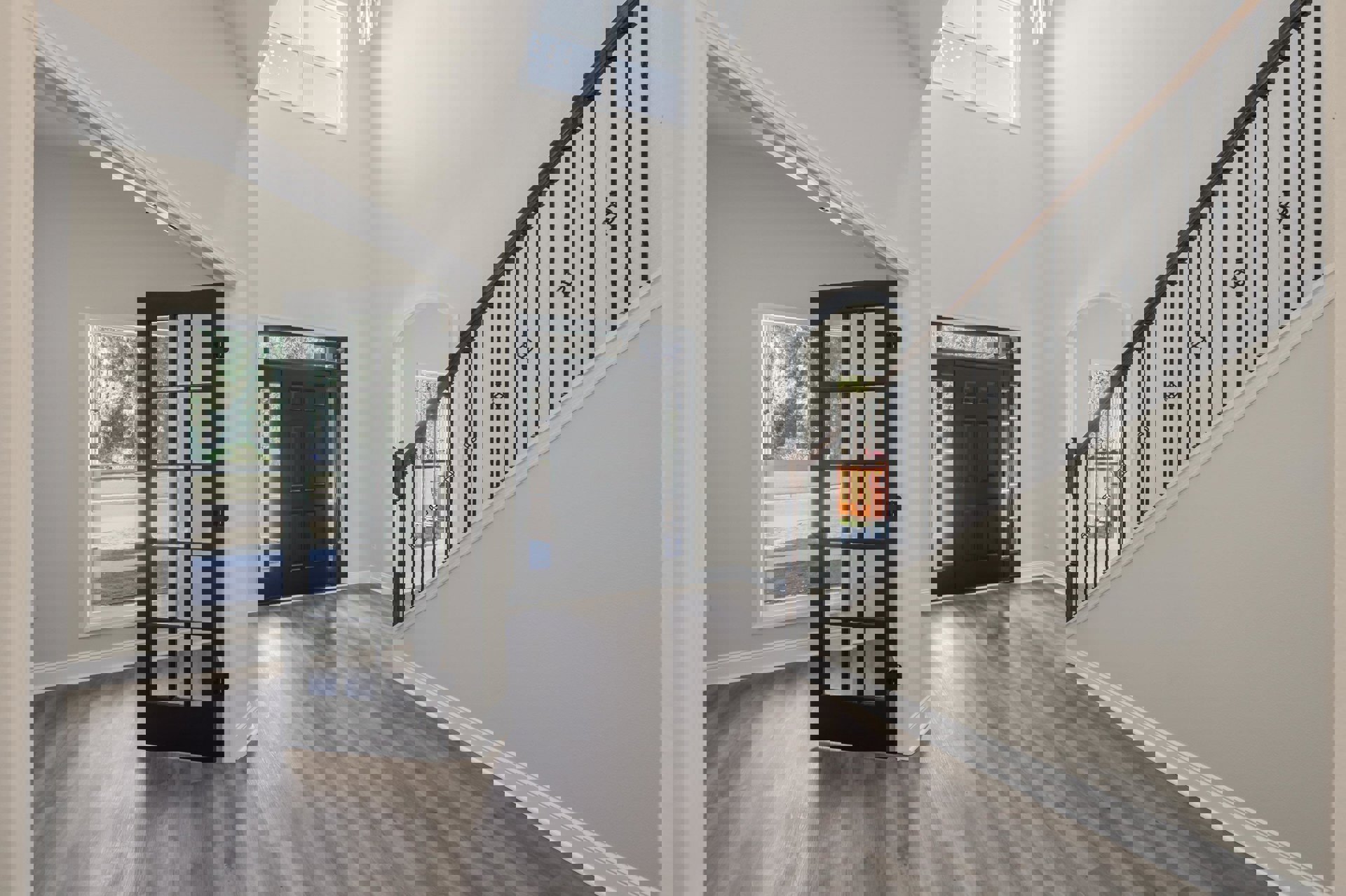 Hallway with light wood flooring, black door with glass panels, staircase featuring metal railings, and large window overlooking forested street