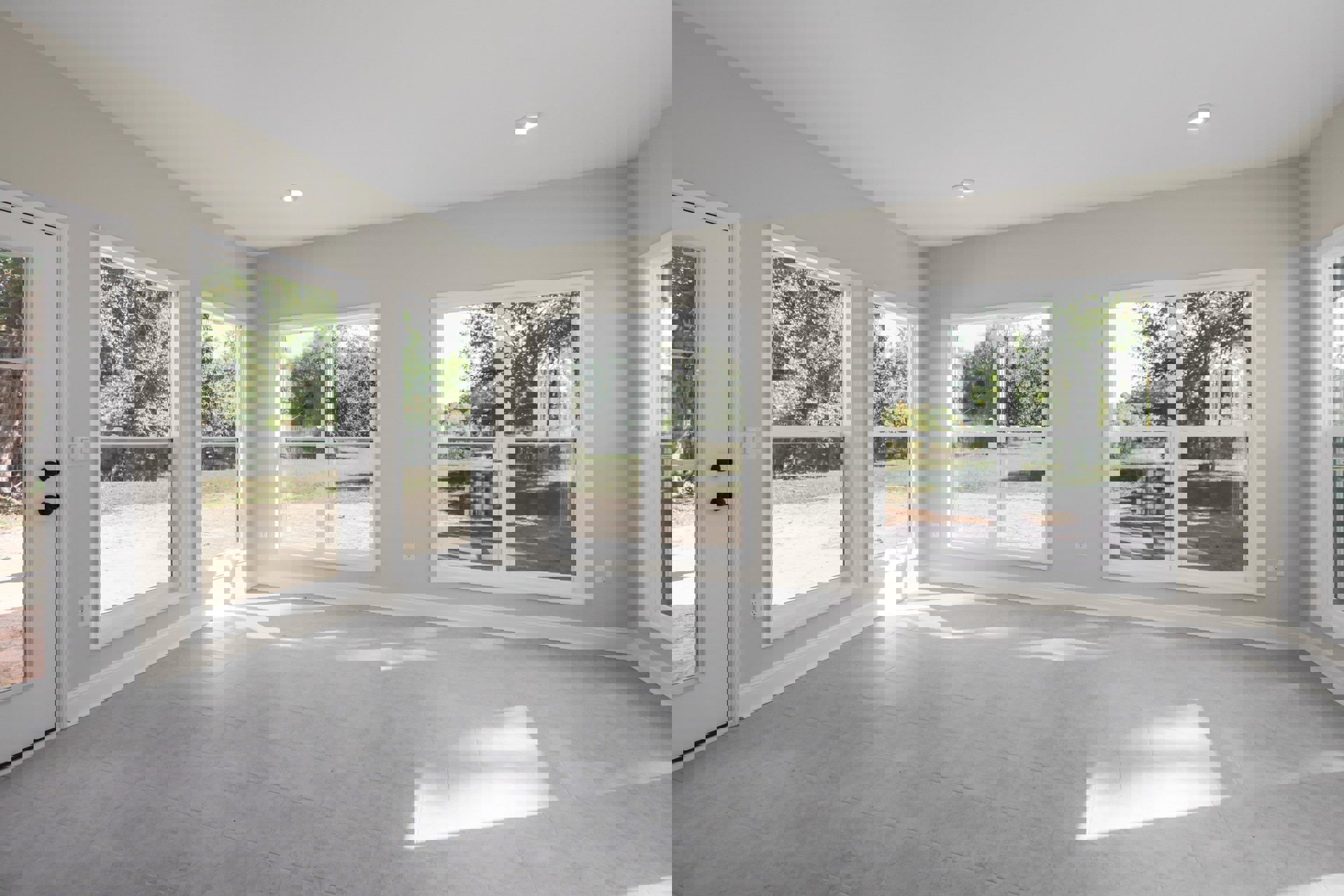 Spacious room featuring large windows, white tile flooring, and a view of green trees under a cloudy sky