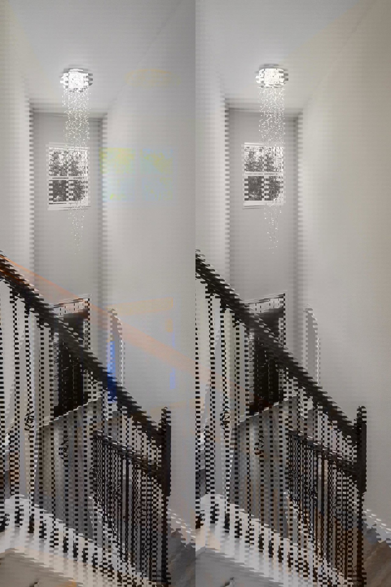 Curved staircase with black railing beneath a modern chandelier, white-framed window on the wall, plaster ceiling and walls, light fixture with white shade, hardwood floor