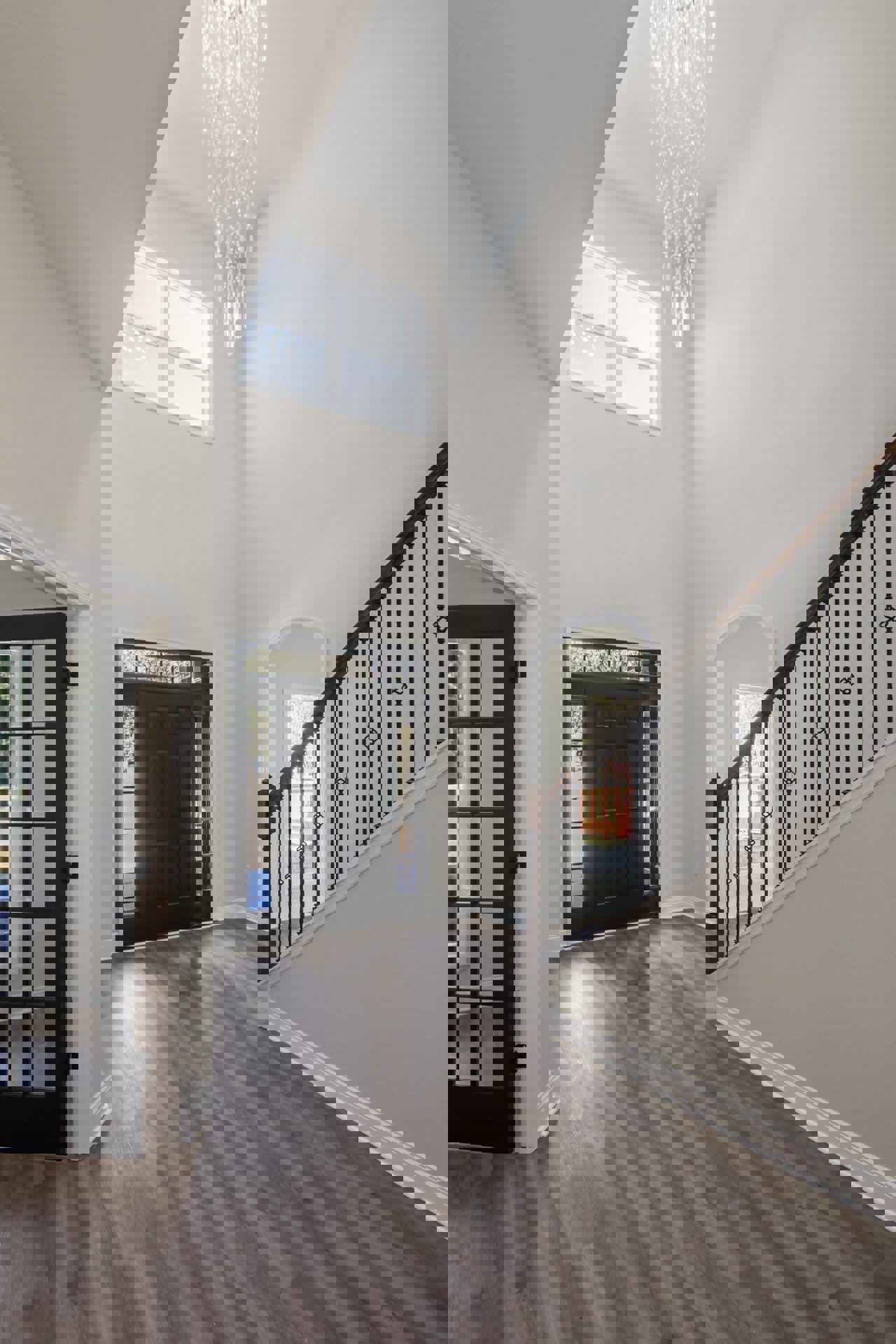 Wood staircase with black metal railings, glass-paneled black front door, chandelier overhead, light wood flooring, white walls with crown molding